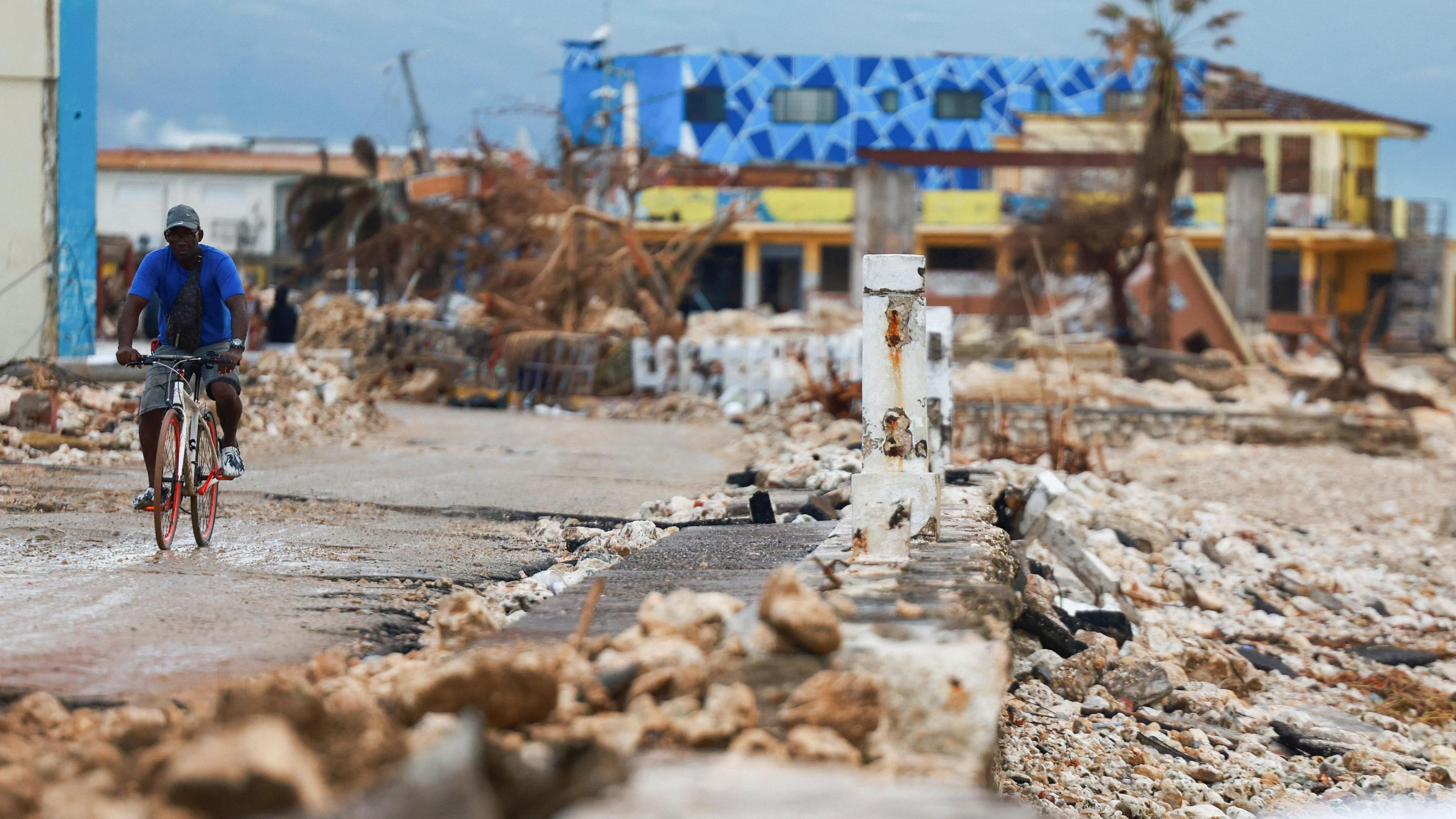 A man rides a bicycle along a metalled road, past damaged buildings in the aftermath of Hurricane Melissa, in Black River, Jamaica,