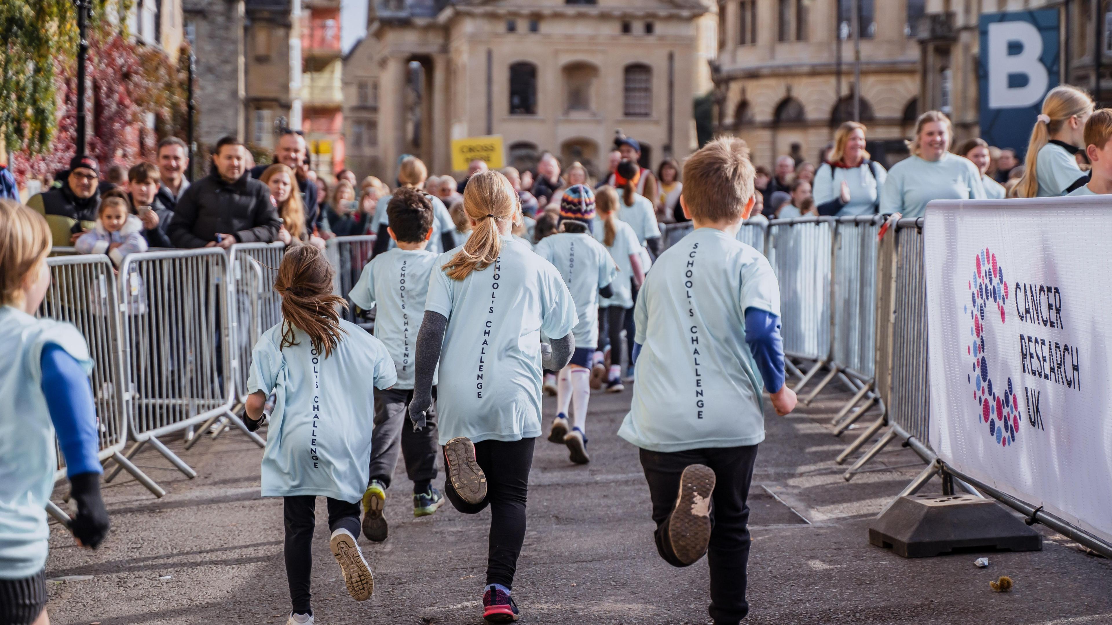 A group of children, all wearing light blue t-shirts, running between large crowds wither side of them.