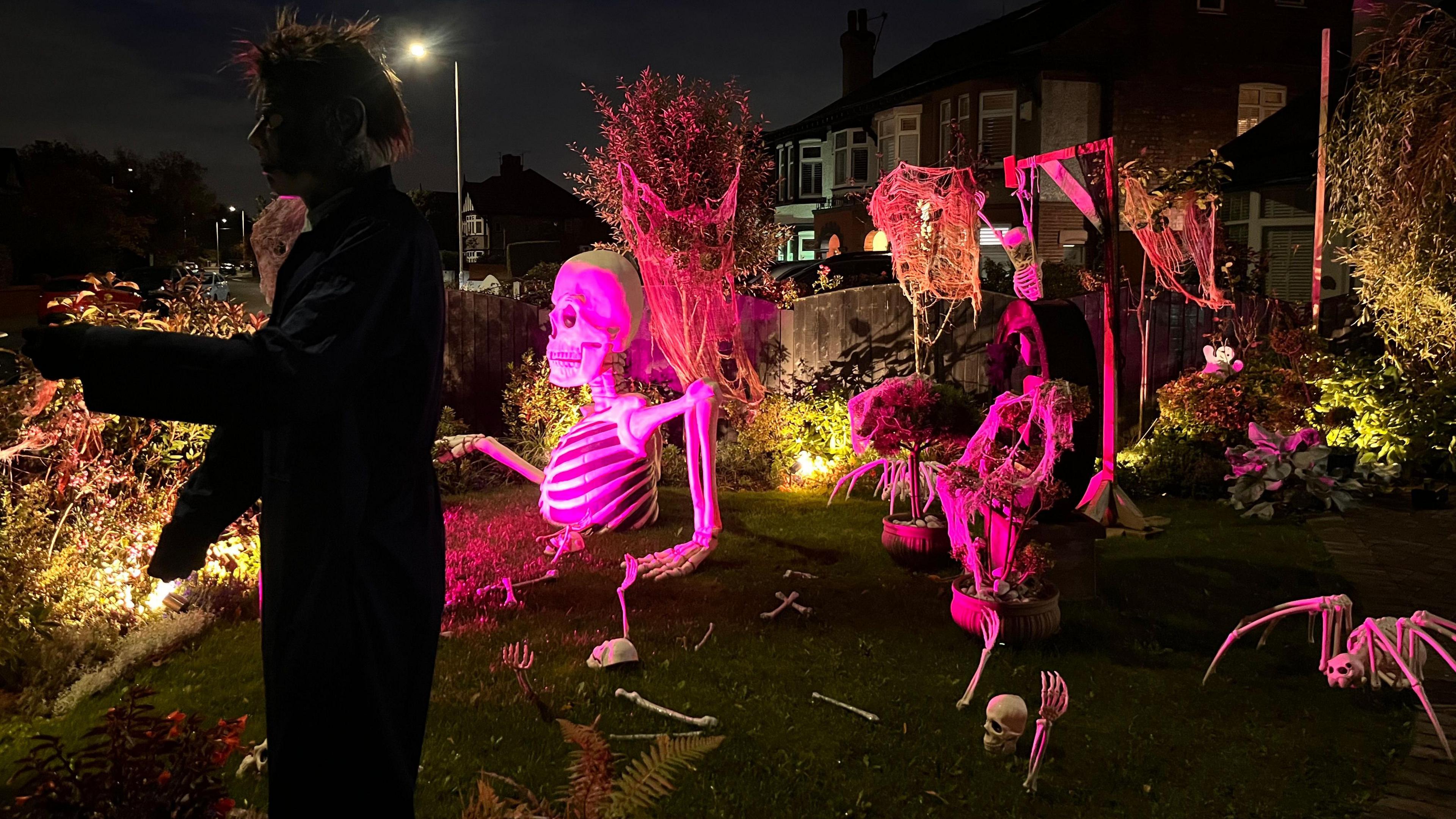 A mannequin depicting Michael Myers from the Halloween films is dressed in an overall and has short spiky hair. A number of skeletons are nearby, including one on gallows.