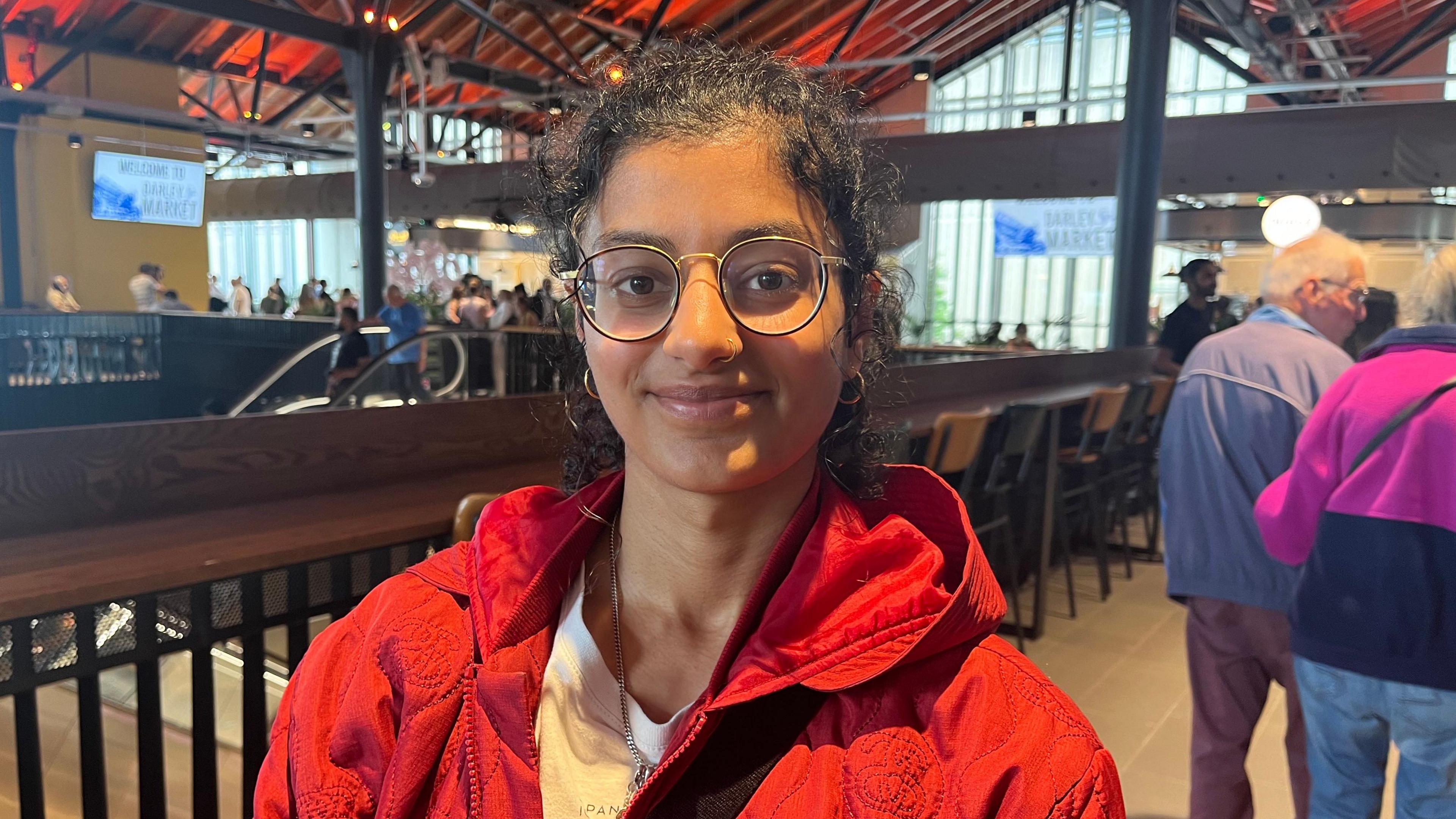 Woman wearing glasses and red coat standing inside market.