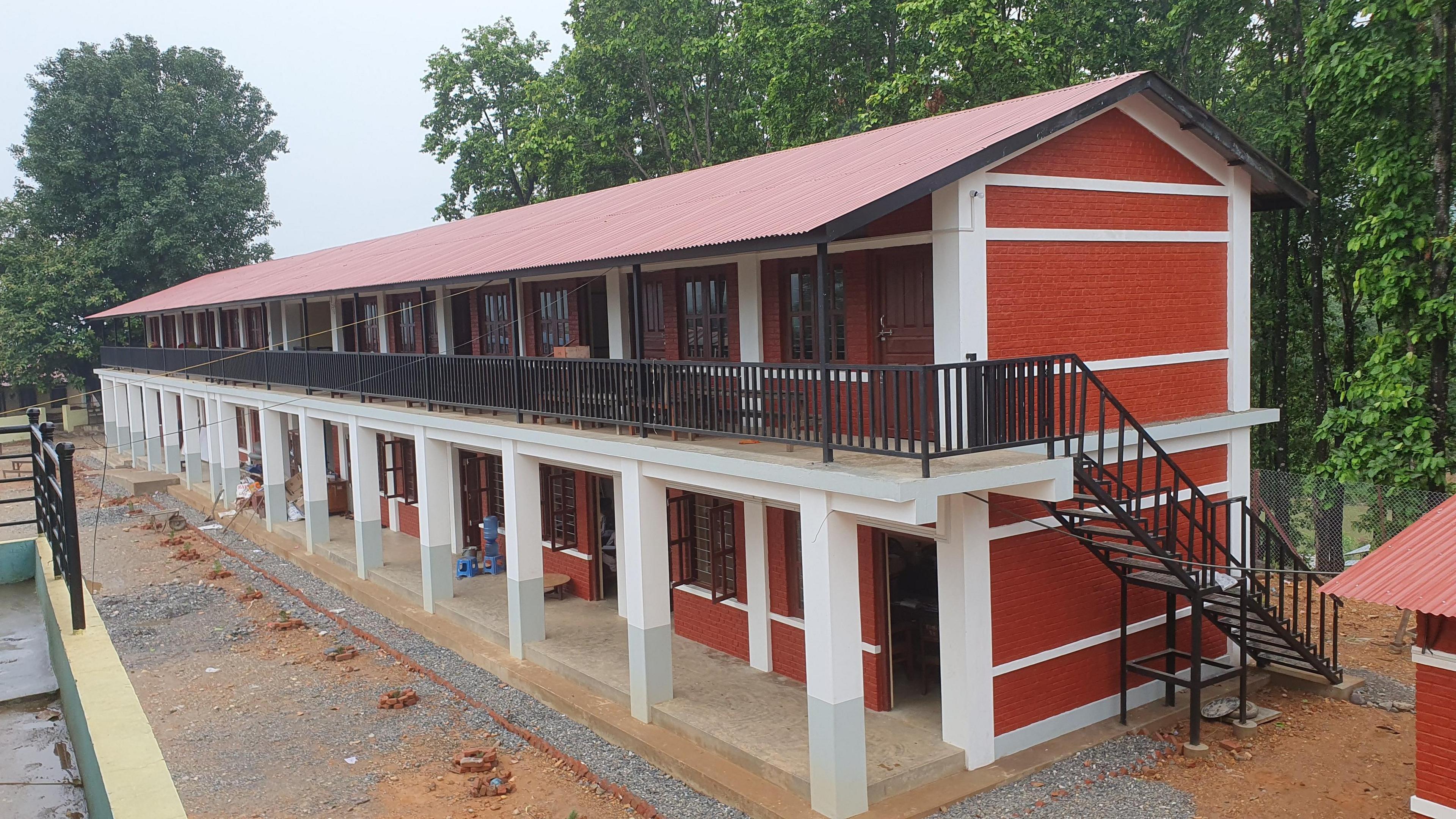 A two storey building made with red bricks and white concrete, with metal railings on the first floor.