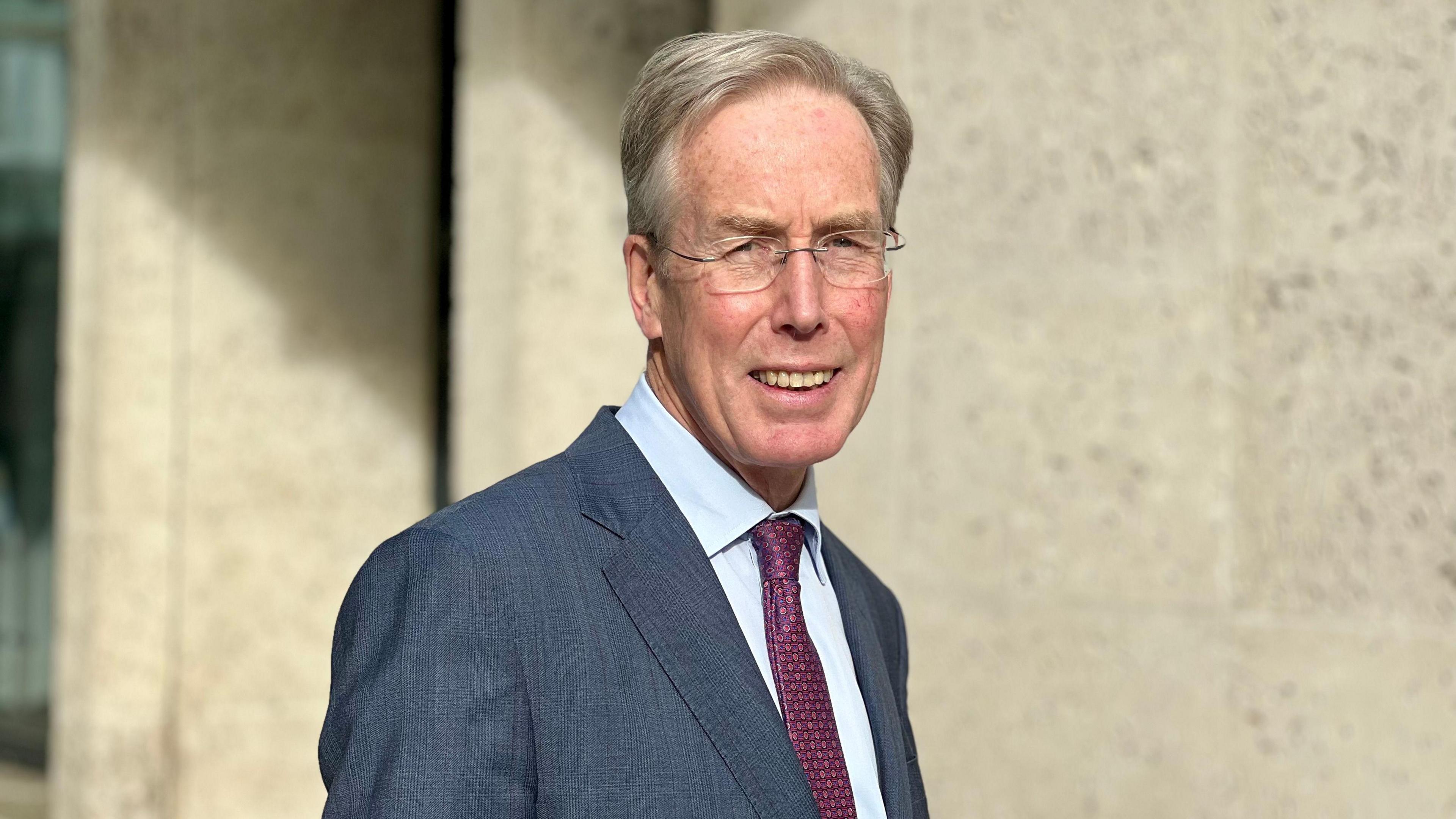 A picture of Sir David Behan, the OfS chairman, in a navy suit with dark purple tie. He's looking and smiling at the camera.