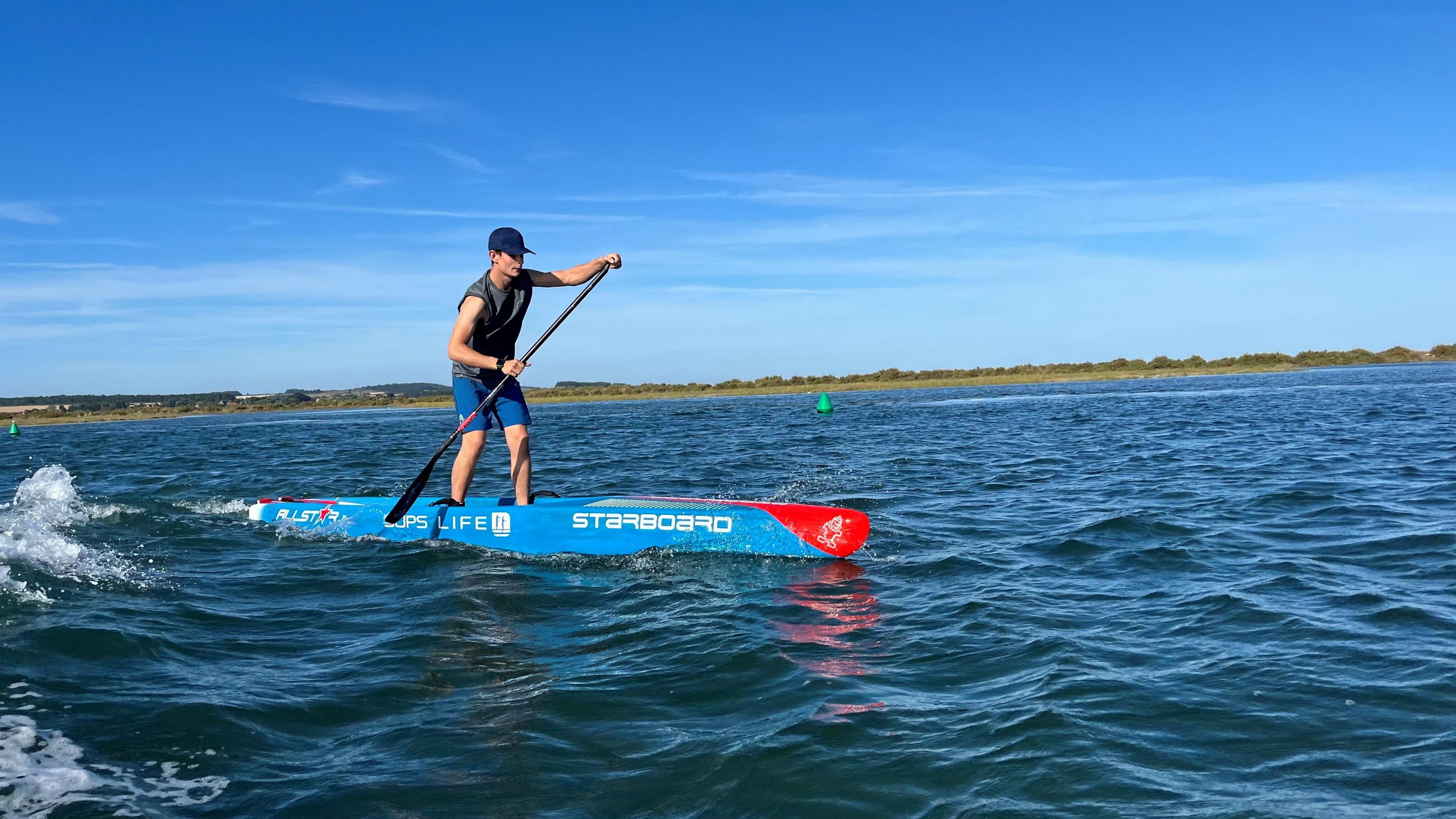 Charlies riding and racing over the open waves. He wrestles to keep his balance on a sunny day on Burnham Overy Creek in gorgeous sunlight with deep blue skies behind him.