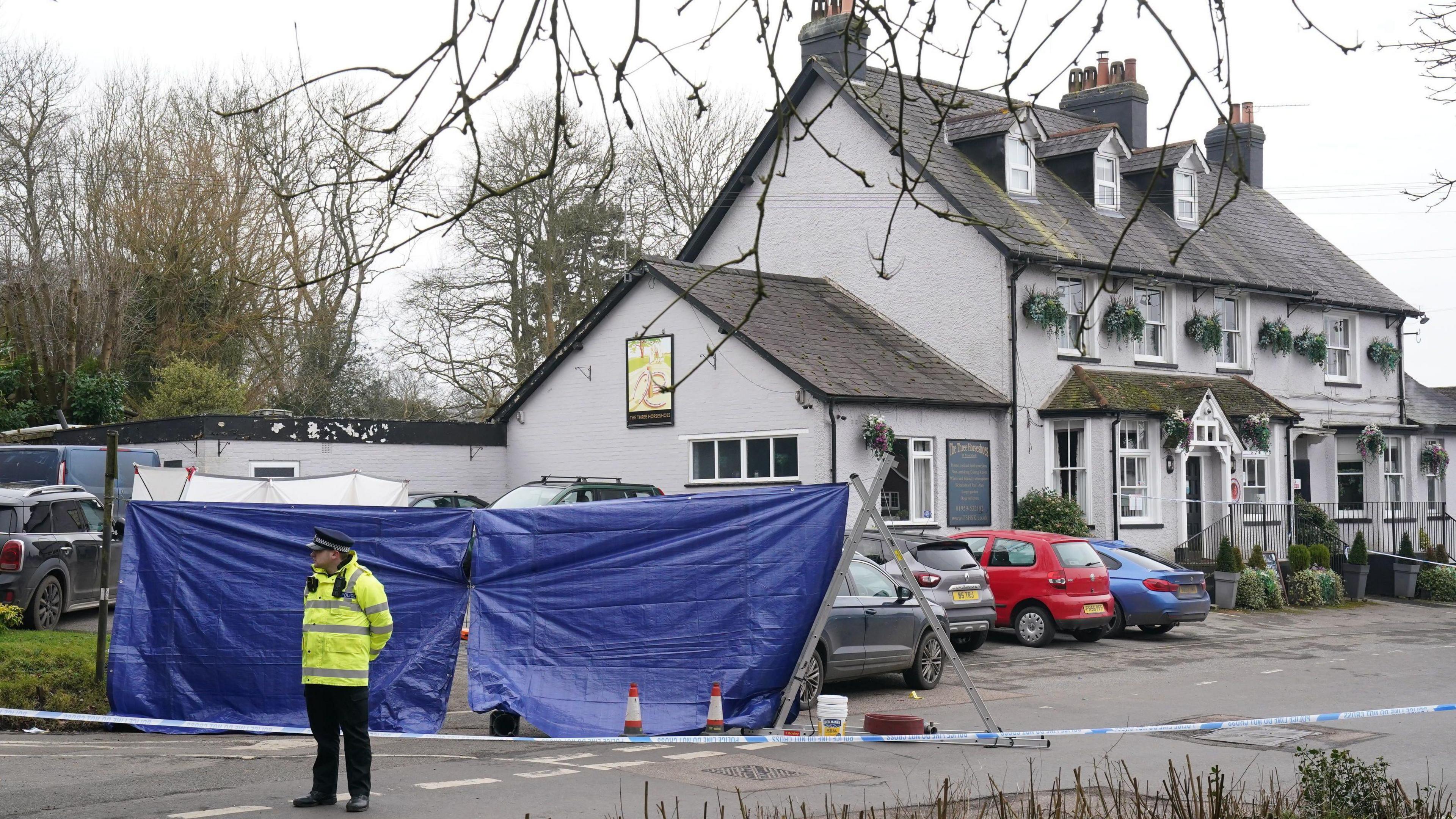 A police officer stands outside the Three Horseshoes pub in Knockholt.