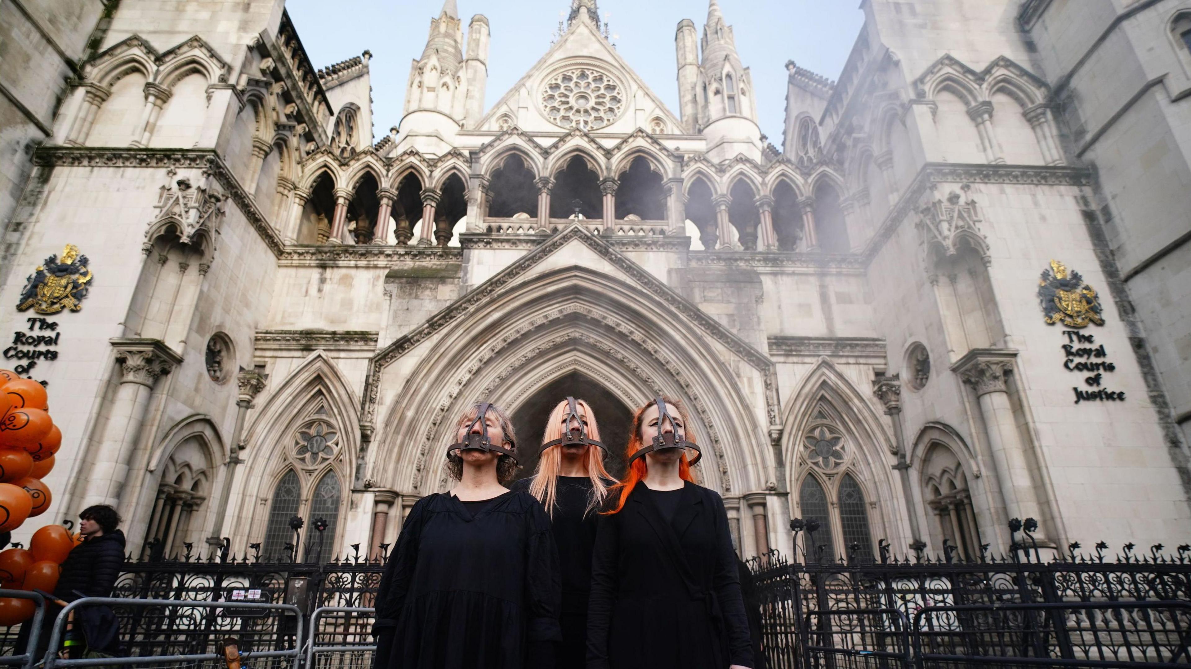 Three female campaigners dressed in black wearing shackles on their heads outside the Royal Courts of Justice in London