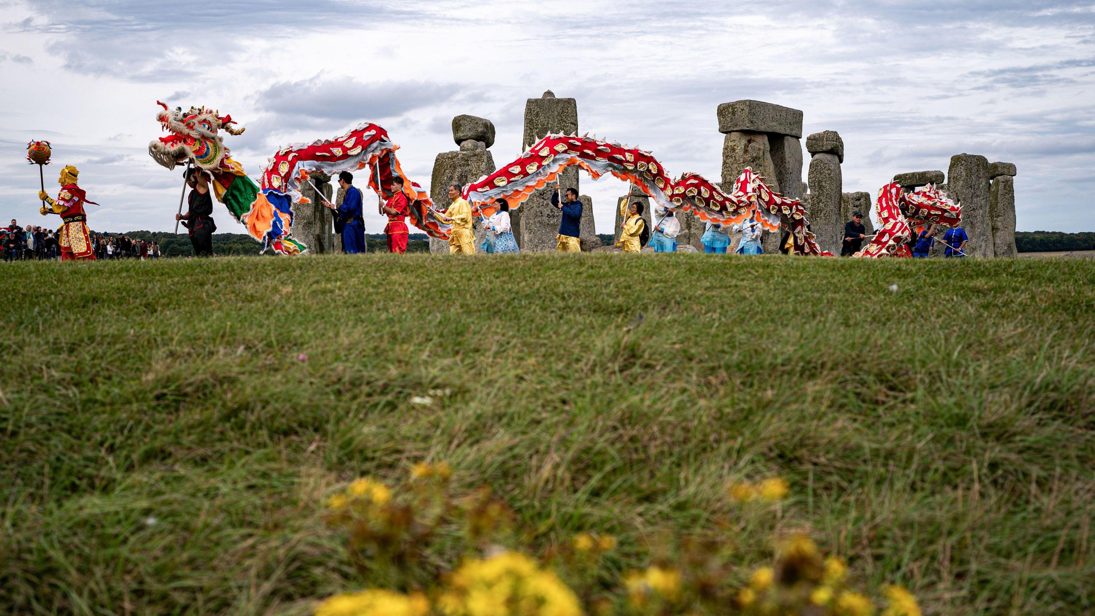 Group of people at the Chinese Mid-Autumn Festival at Stonehenge. They are carrying a large dragon puppet past the stones. 