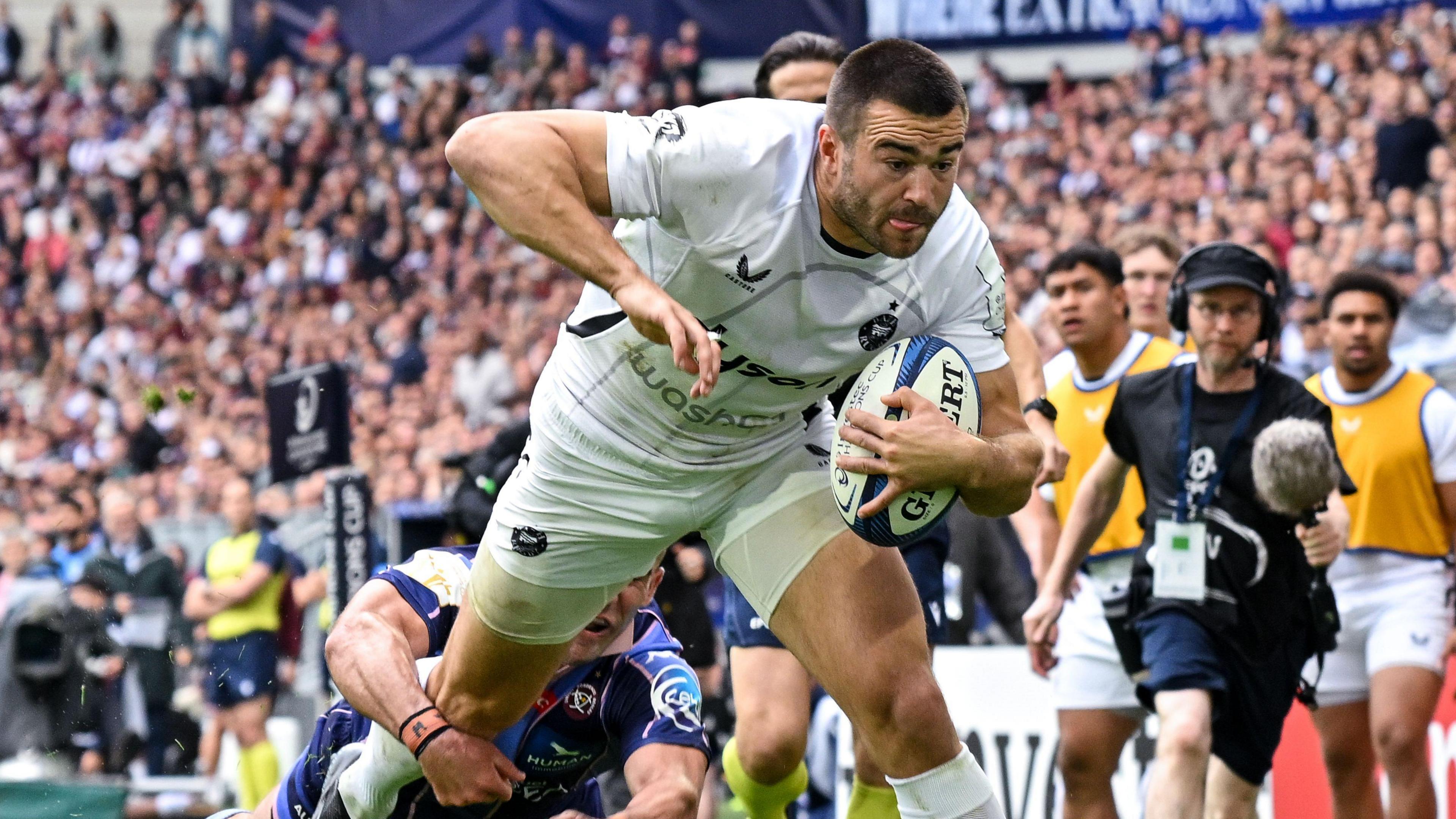 Will Muir dives towards the line with the ball under his left arm as a Bordeaux player wraps his arm around his right leg in an attempt to prevent a try during their Champions Cup match
