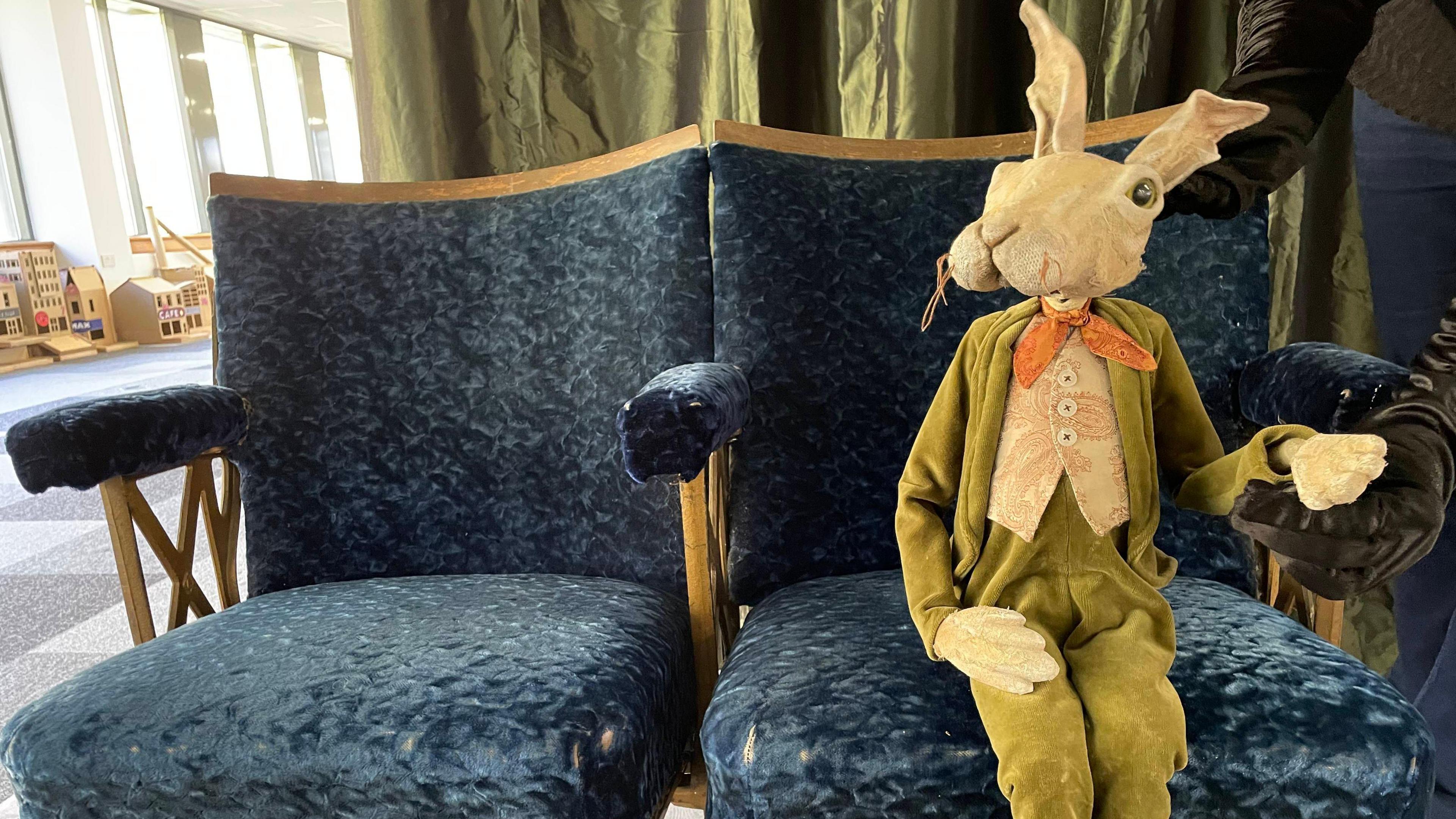 The same rabbit puppet sitting on a blue, velvet theatre chair.