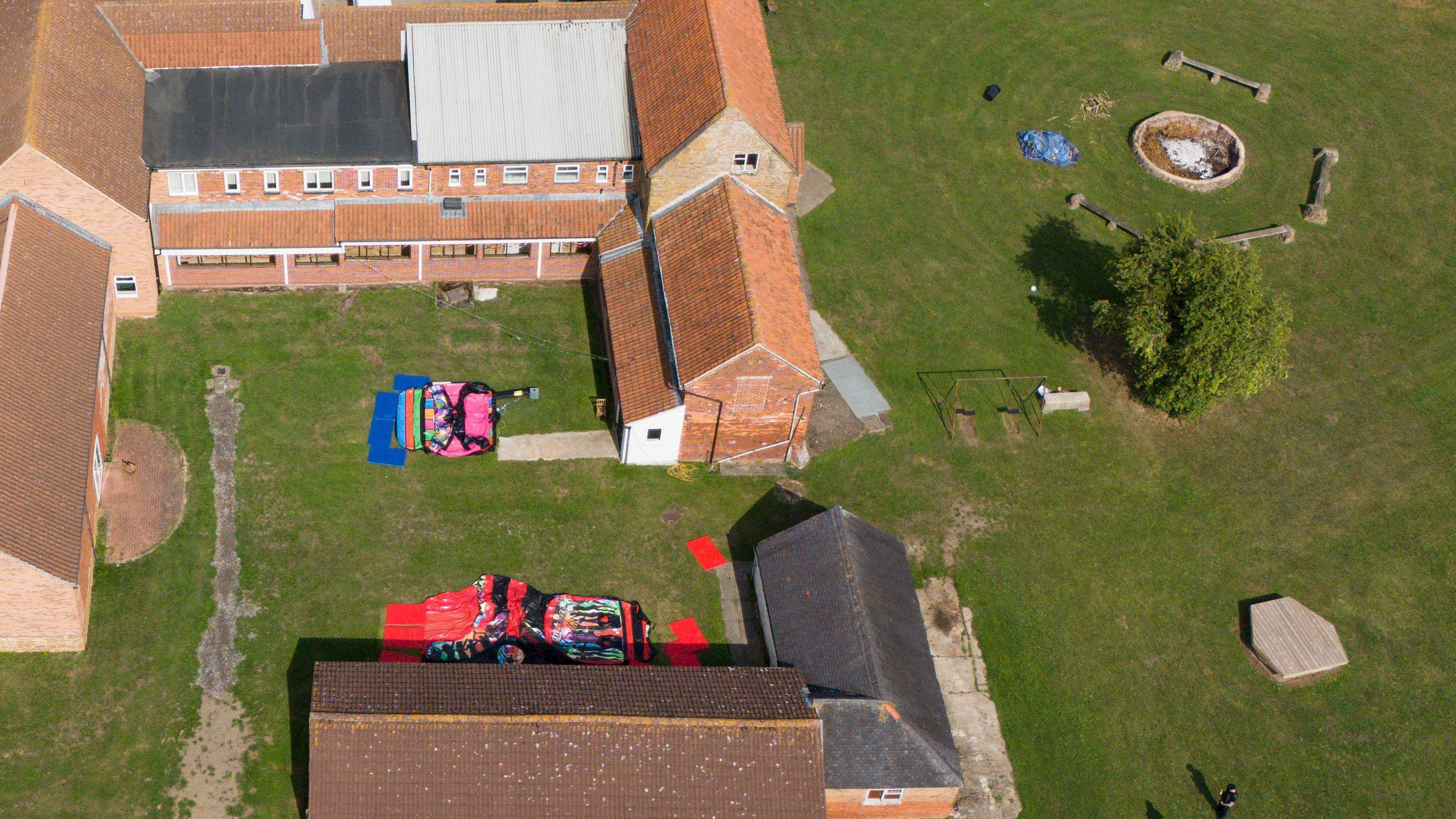The site of a summer camp is pictured with several sleeping bags lying on grass inside the courtyard of a red brick series of buildings.
