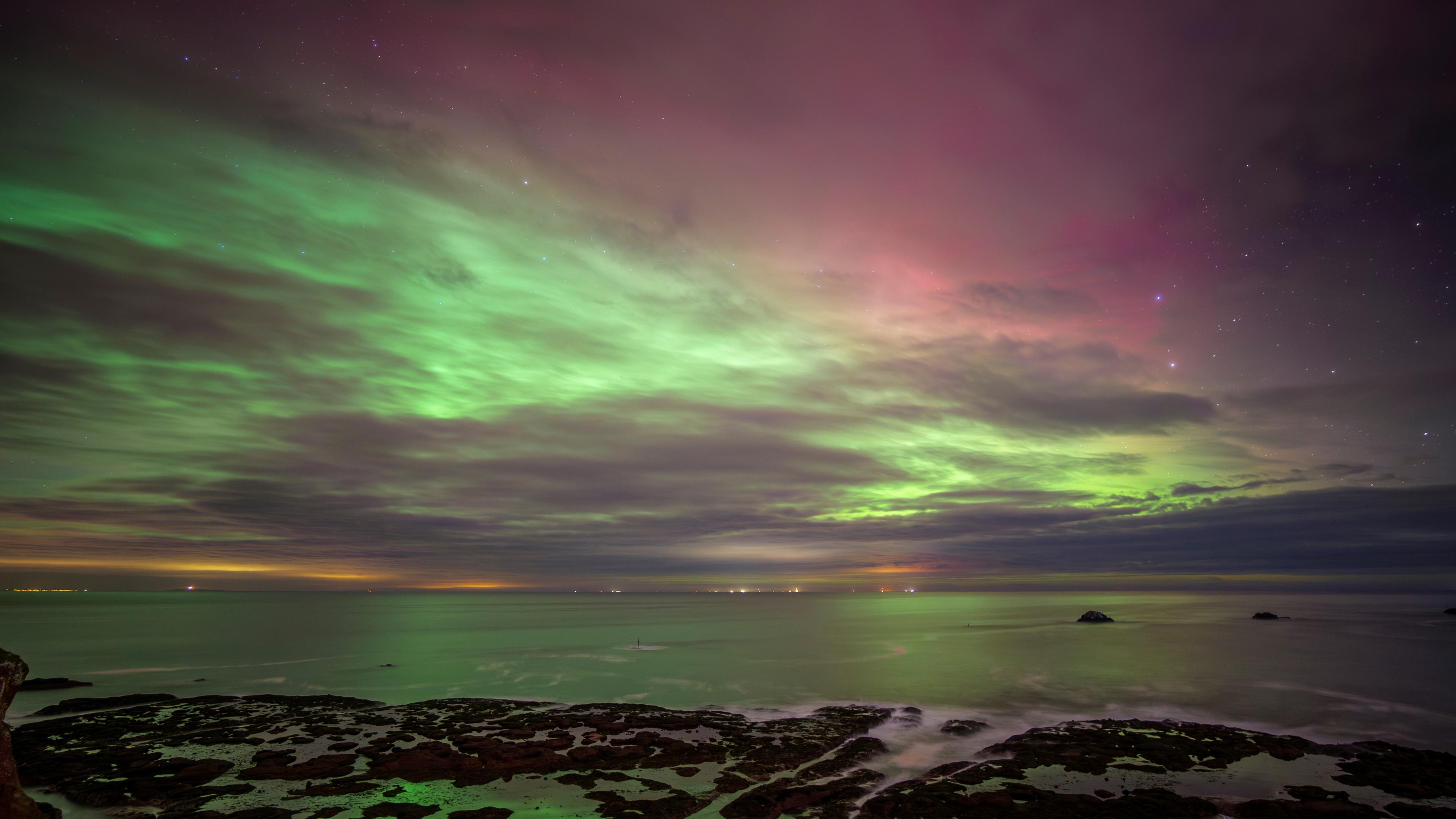 Long exposure of green and red aurora borealis over water