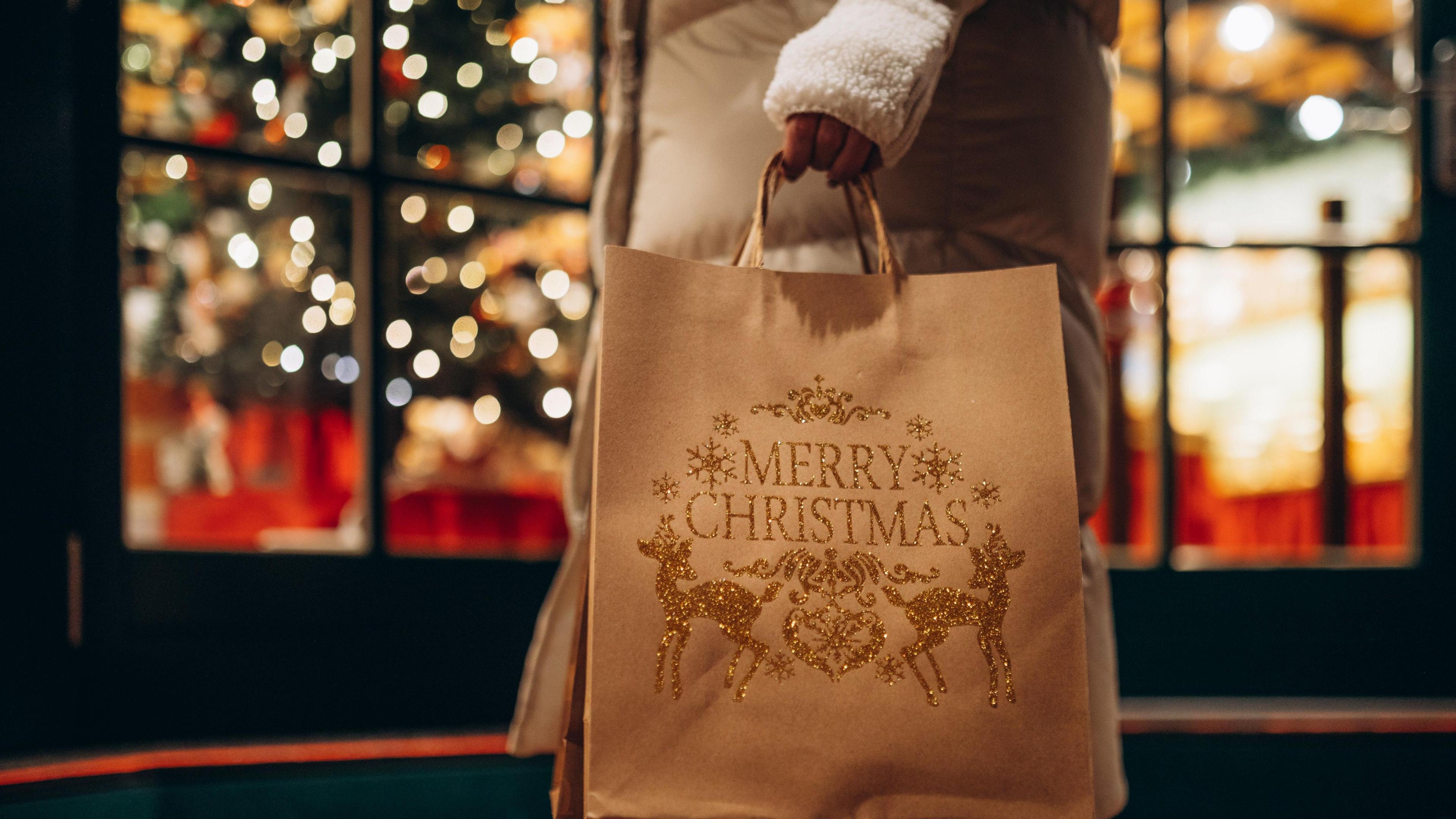 Hand holding Christmas shopping bags against the background of festive storefront.