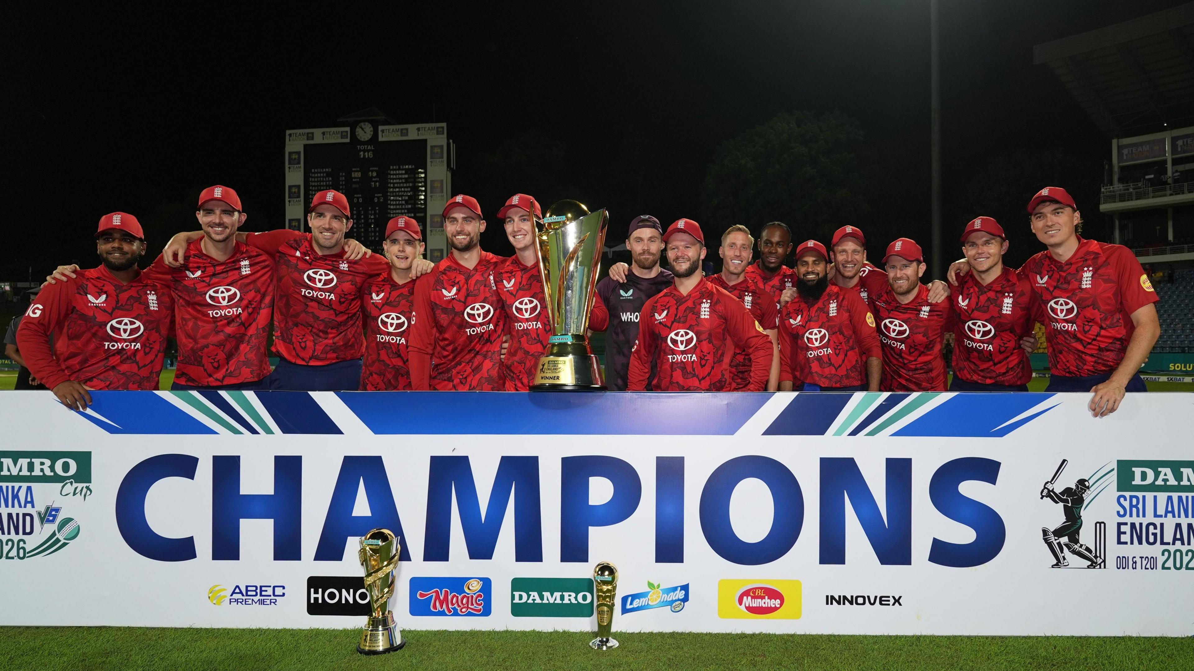 England's squad pose with a trophy, behind a banner saying champions