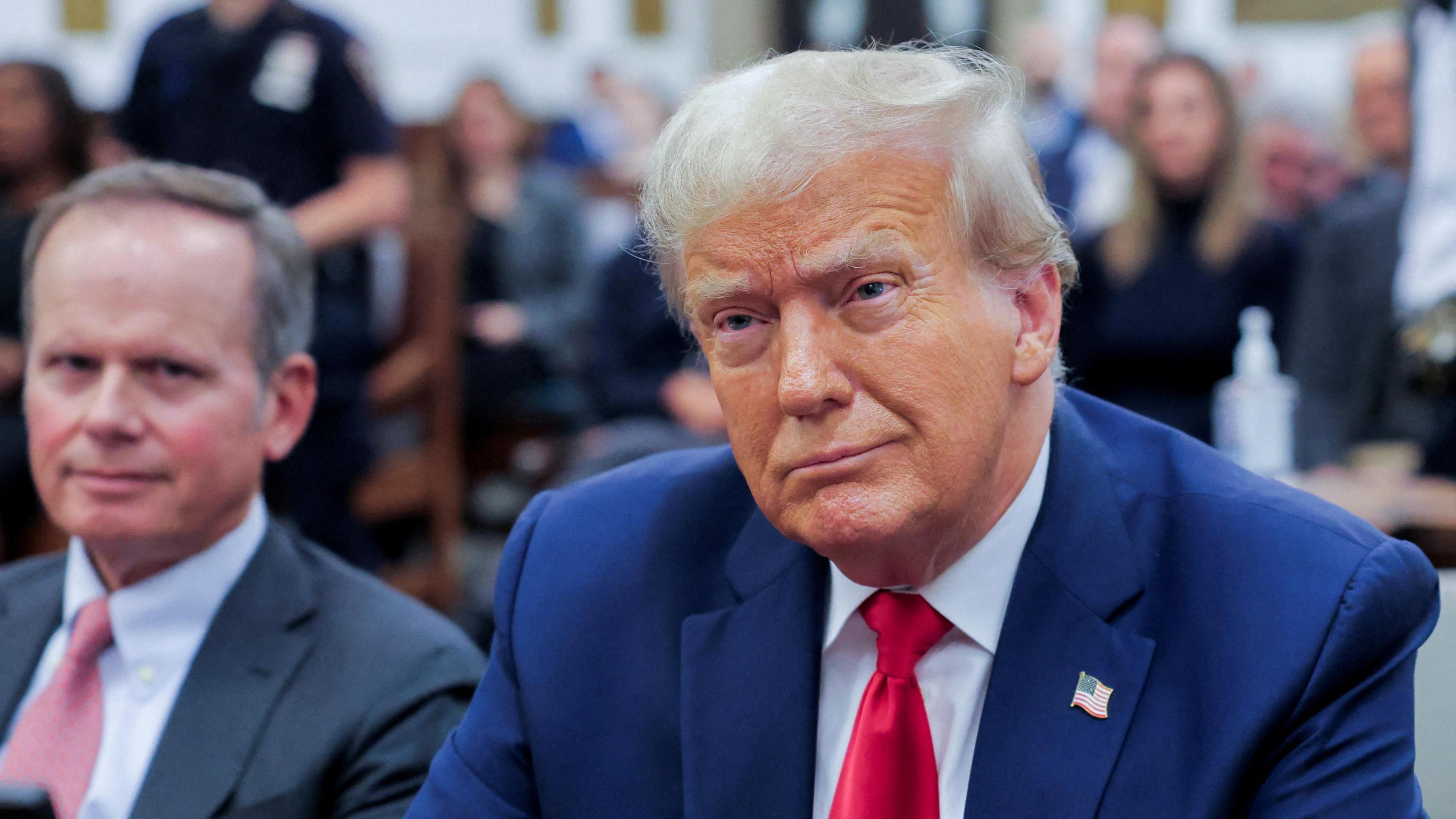 Donald Trump sits wearing a blue suit and red tie