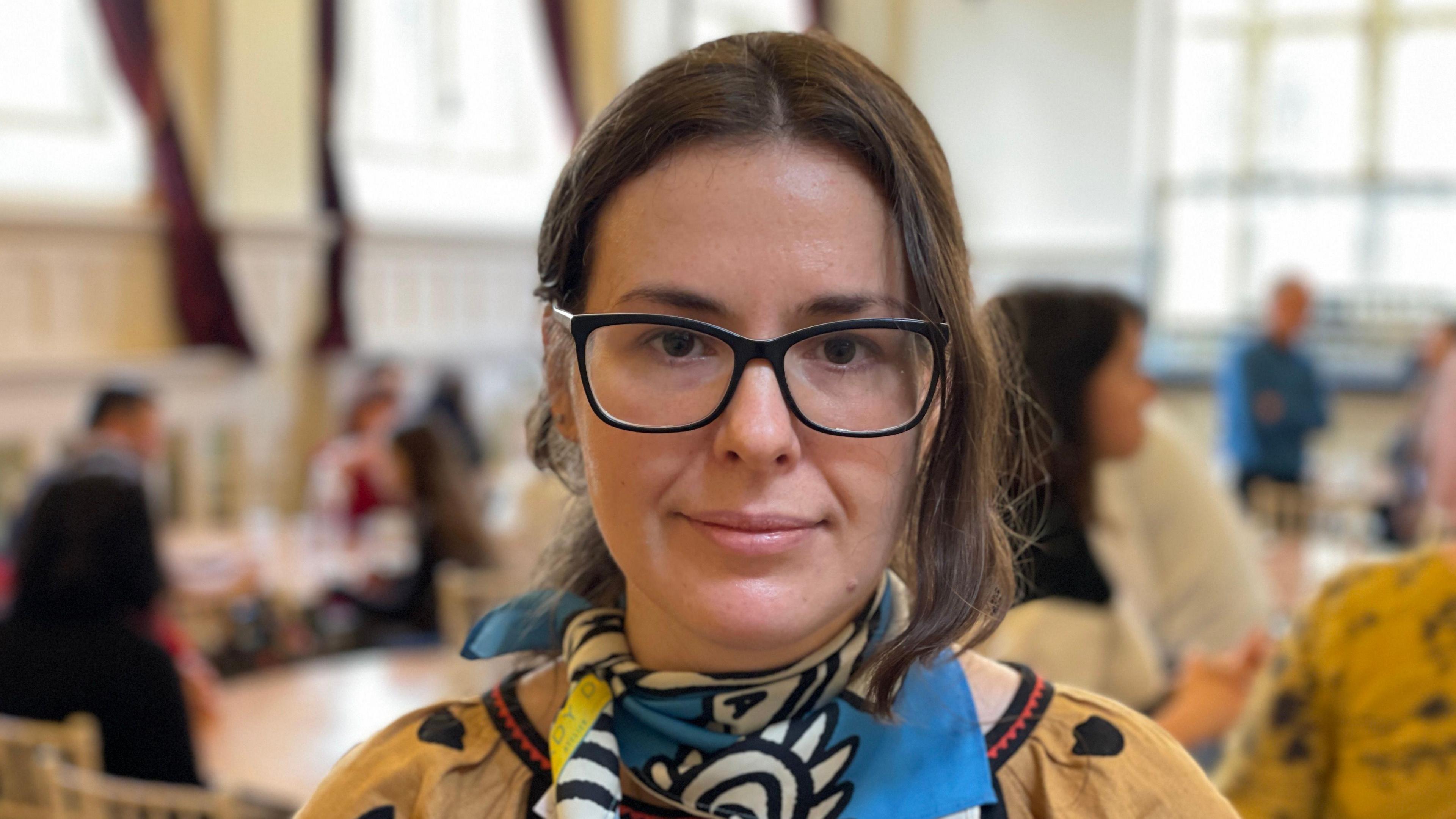 A woman with dark hair and glasses wearing a colourful blue pattered scarf.