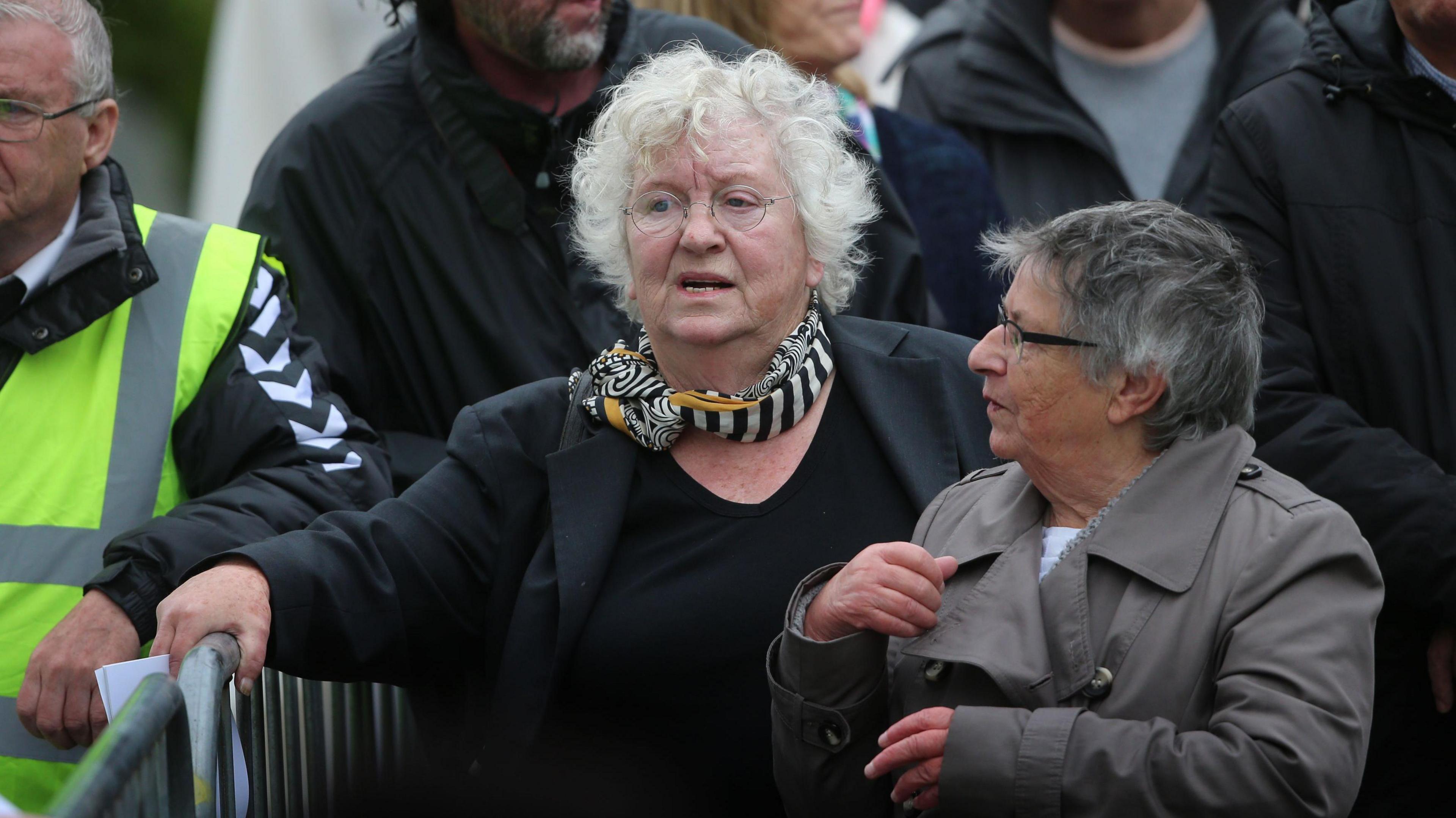 Nell McCafferty walking and talking with with another woman, her hand on a metal barrier 