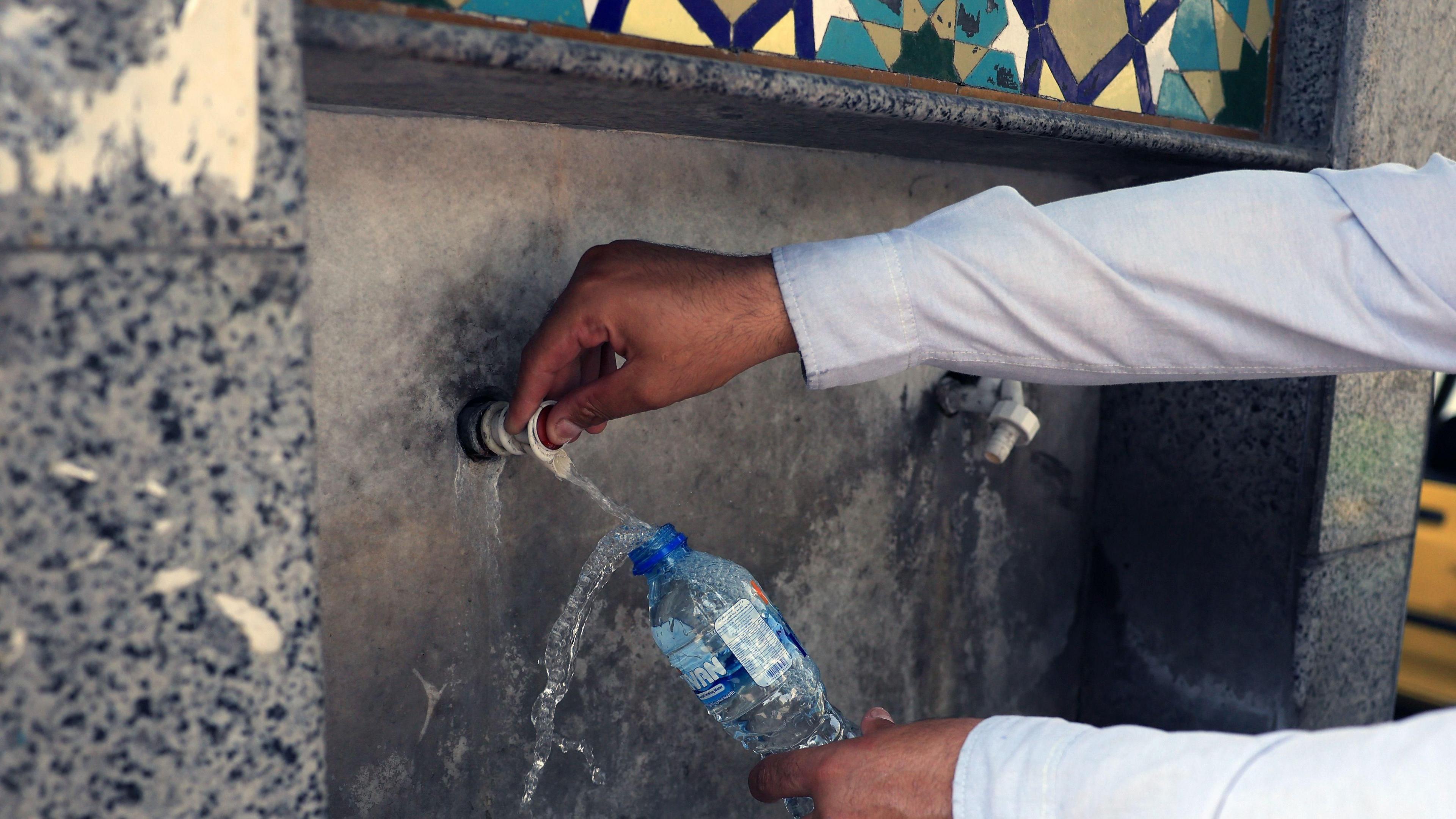 Someone filling up a water bottle from a water fountain in Tehran