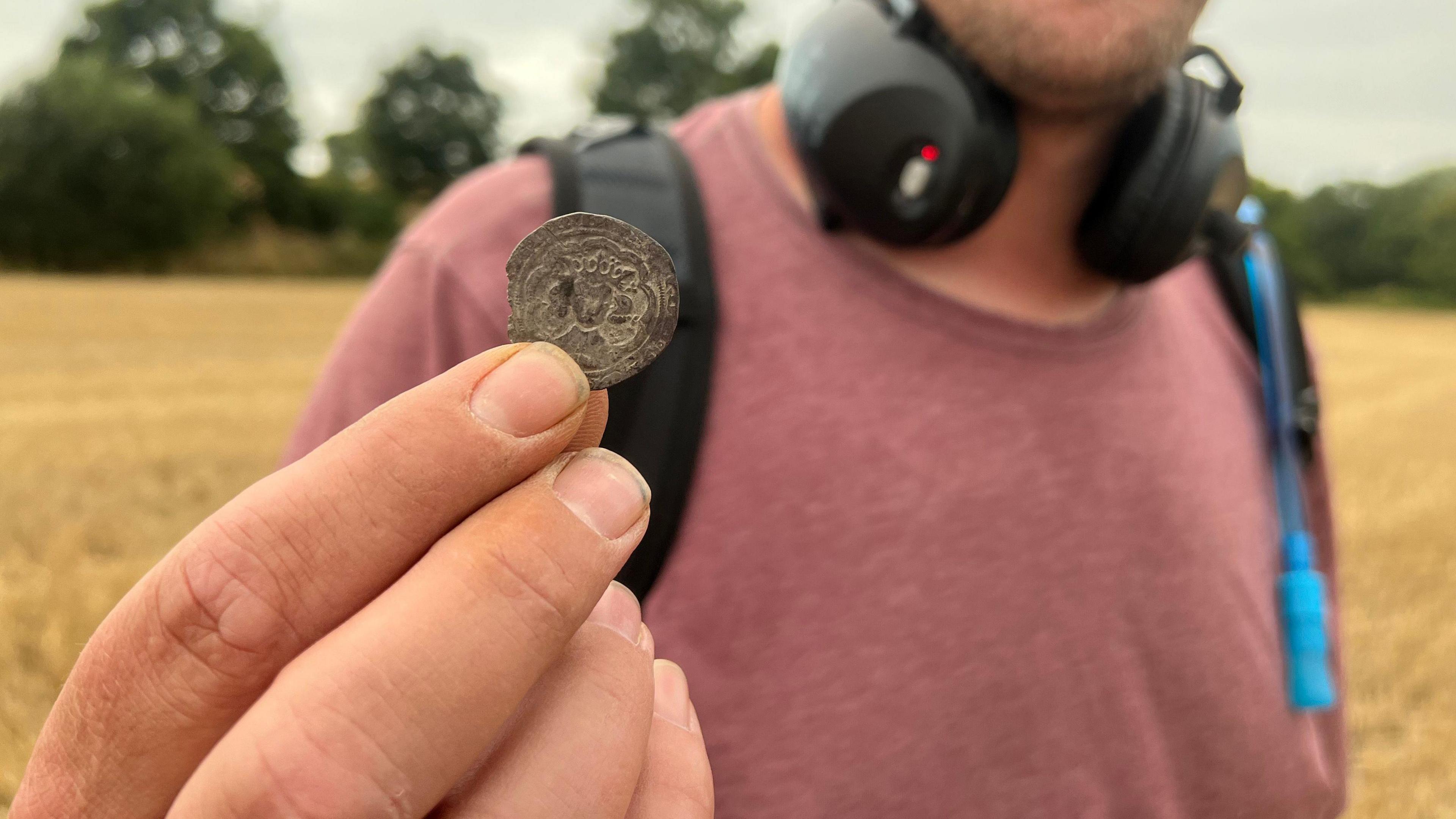 A hold holding up one of the coins found which shows the outline of a king with a crown