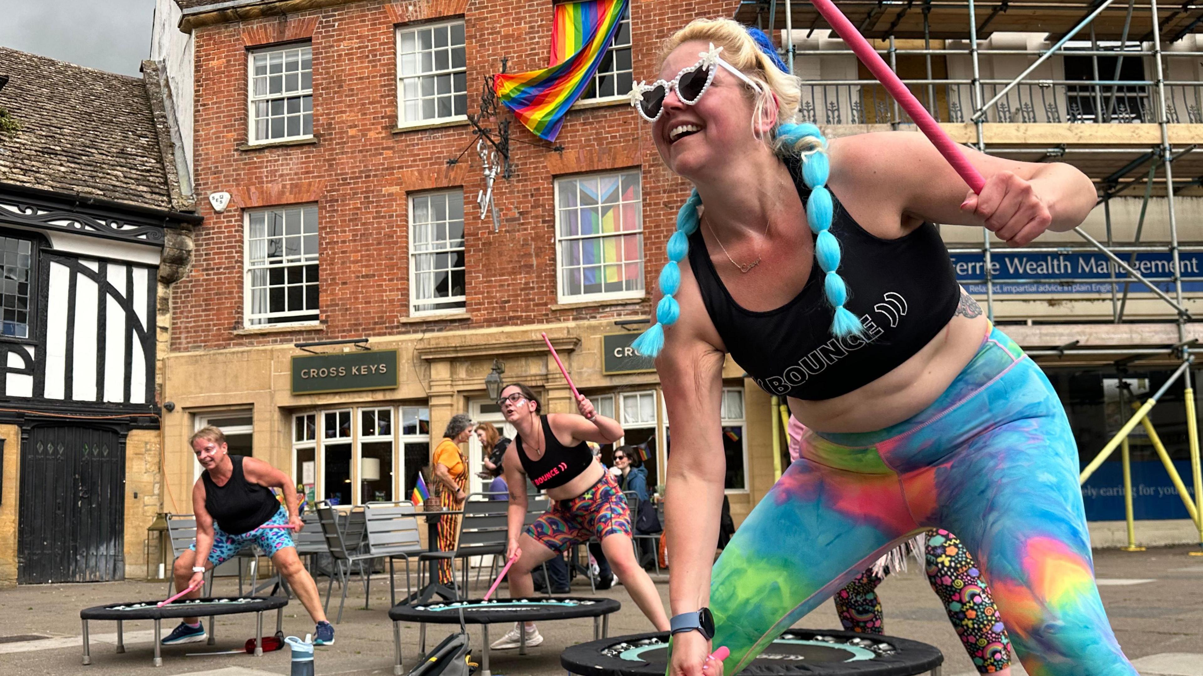 Members of Sherborne Bounce drum on small circular trampolines outside The Cross Keys pub, which has a Pride flag hanging on it