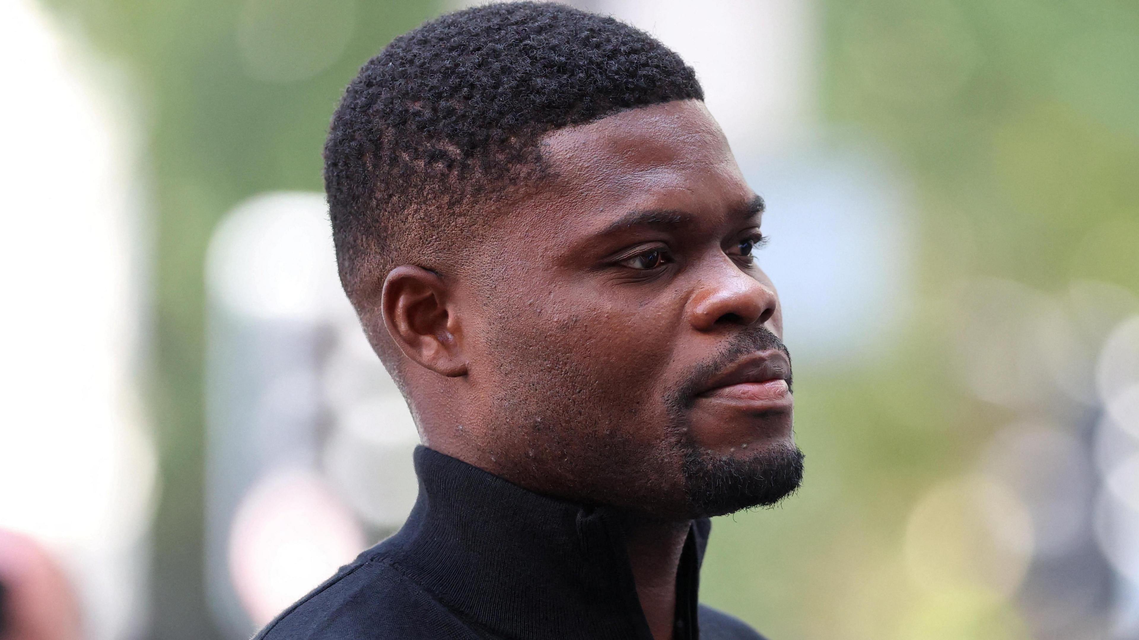 Thomas Partey wears a black zip-up collared sweater as he walks into Westminster Magistrates' Court, in London.