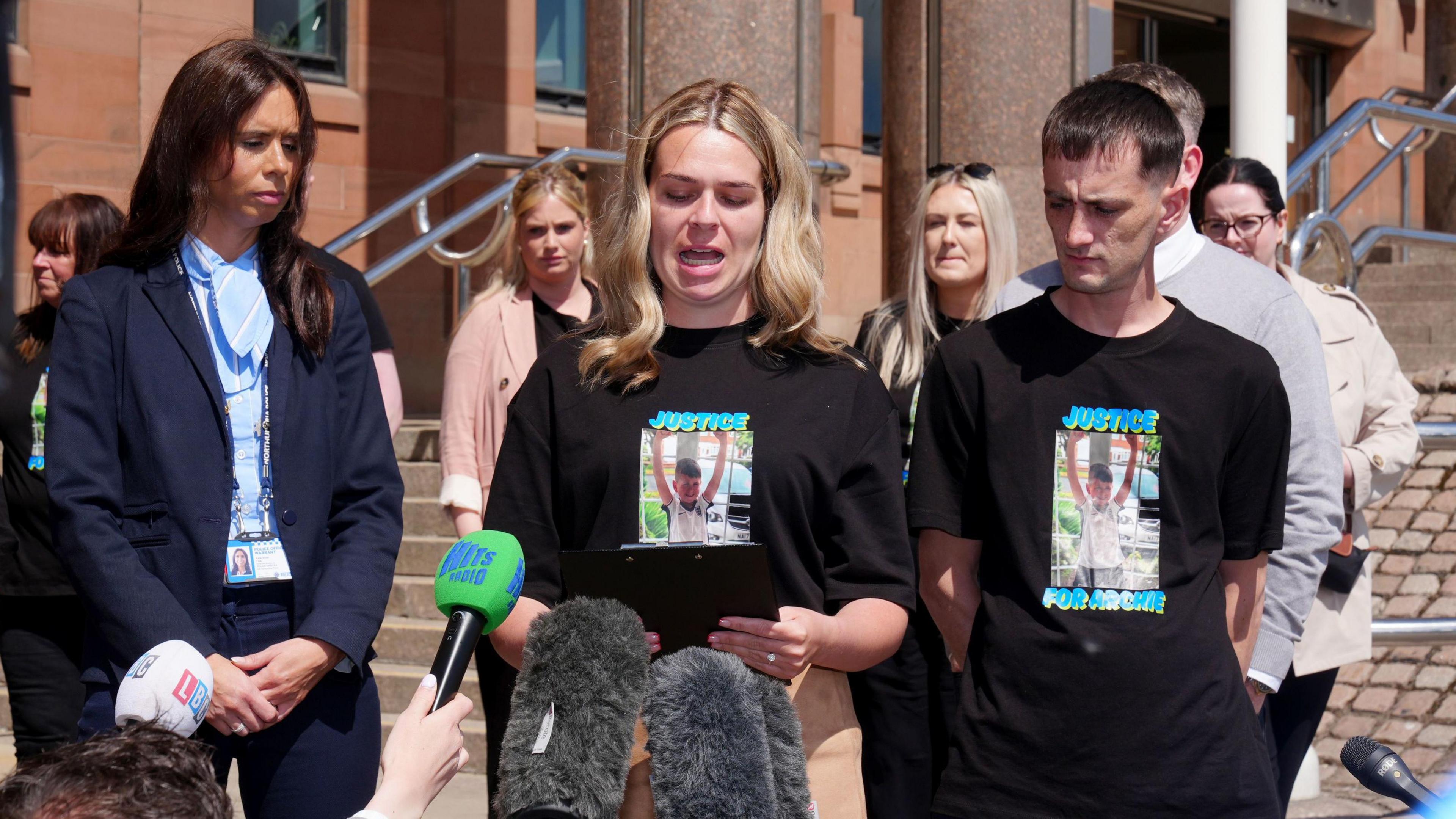 Archi's mum and dad stand side by side outside Newcastle Crown Court as she reads a statement to gathered media.
They are both wearing black t-shirts with a picture of their son and the phrase "justice for Archie" on it.
Katherine Errington has long blond hair, Robbie York has short dark hair.