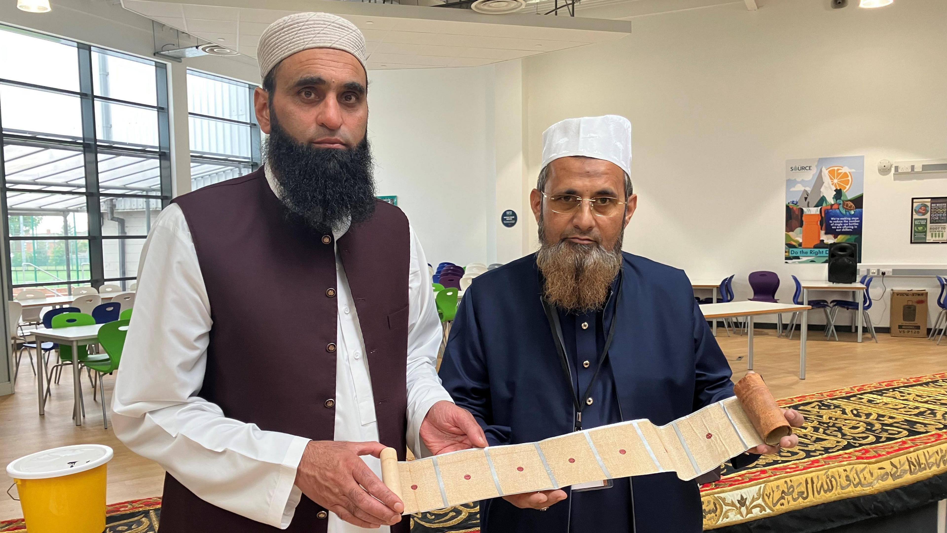 Two men in Islamic clothing with beards holding an ancient Quran scroll [the holy book for Muslims].