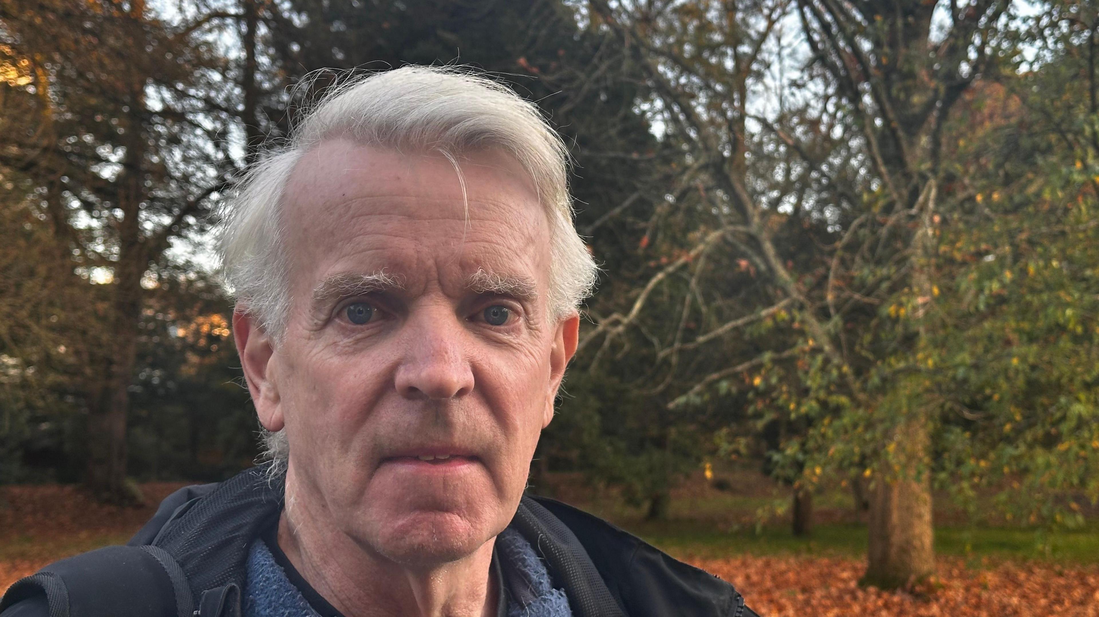 Chris Engel standing in woodland at Bute Park, Cardiff. He as white hair and is wearing a blue jacket