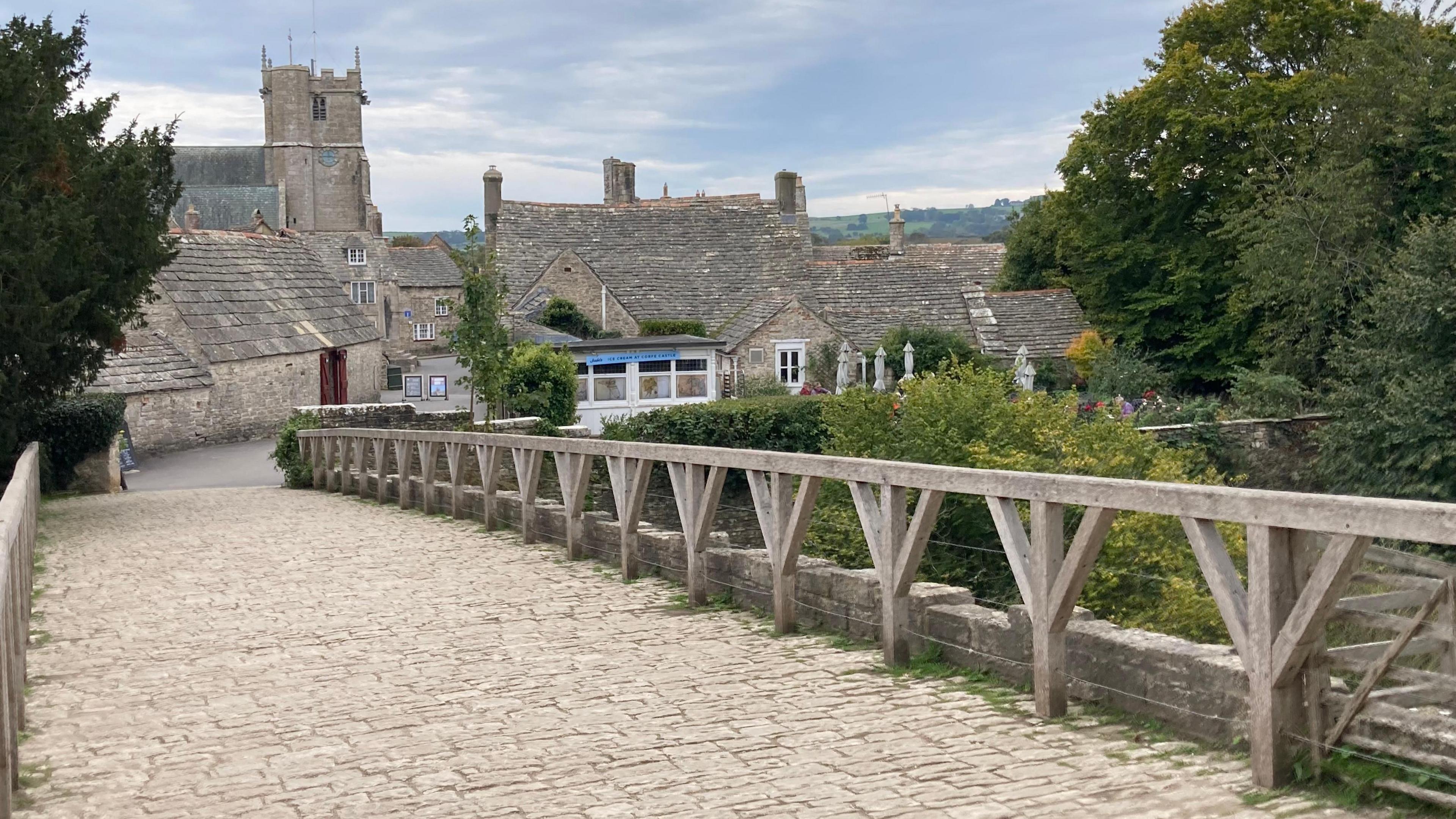 A cobbled bridge leading to a castle in the distance and some old brick housing.