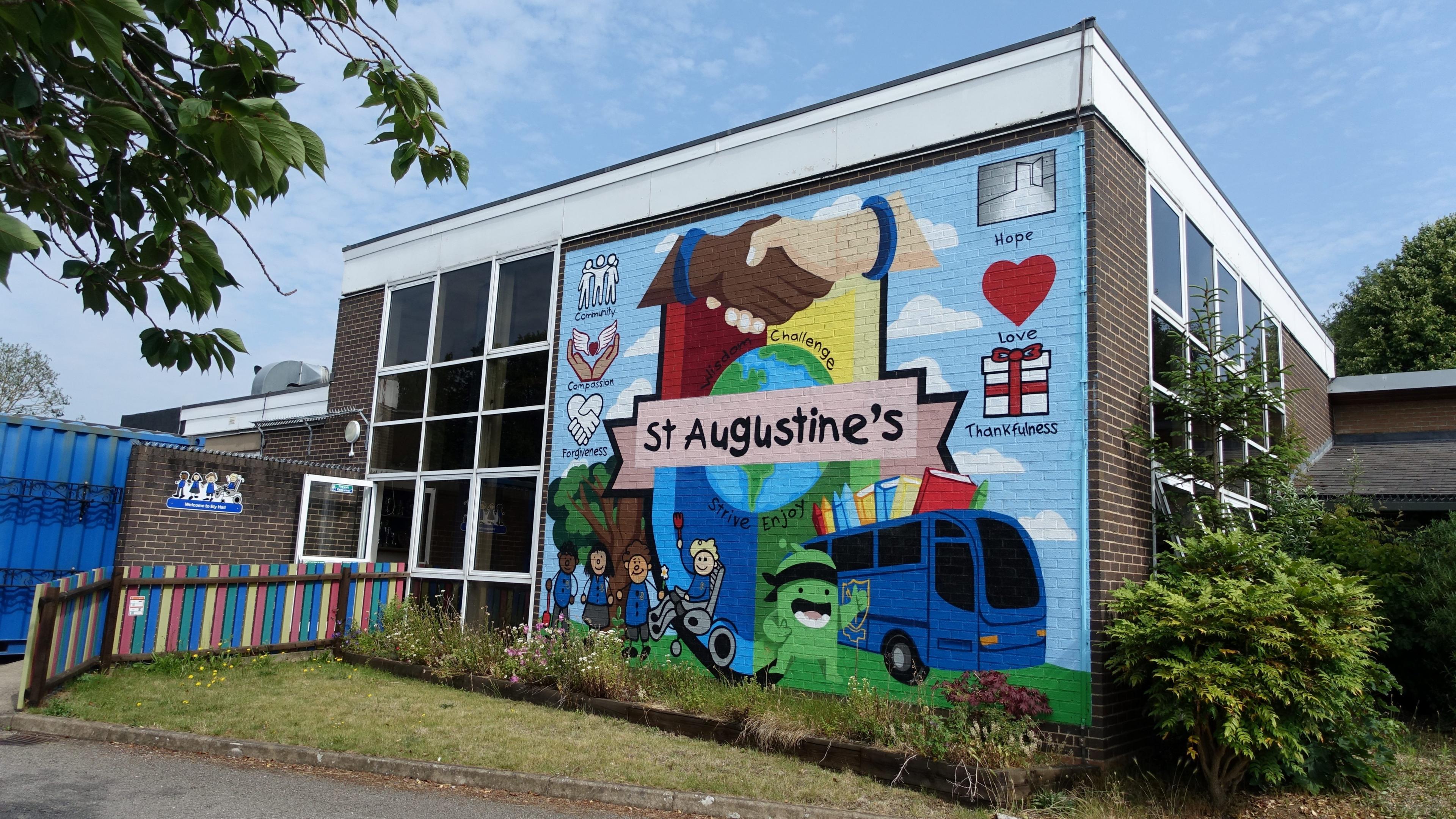 A colourful mural on the side of the school building shows two shaking hands, the book bus and says "St Augustine's" on it.