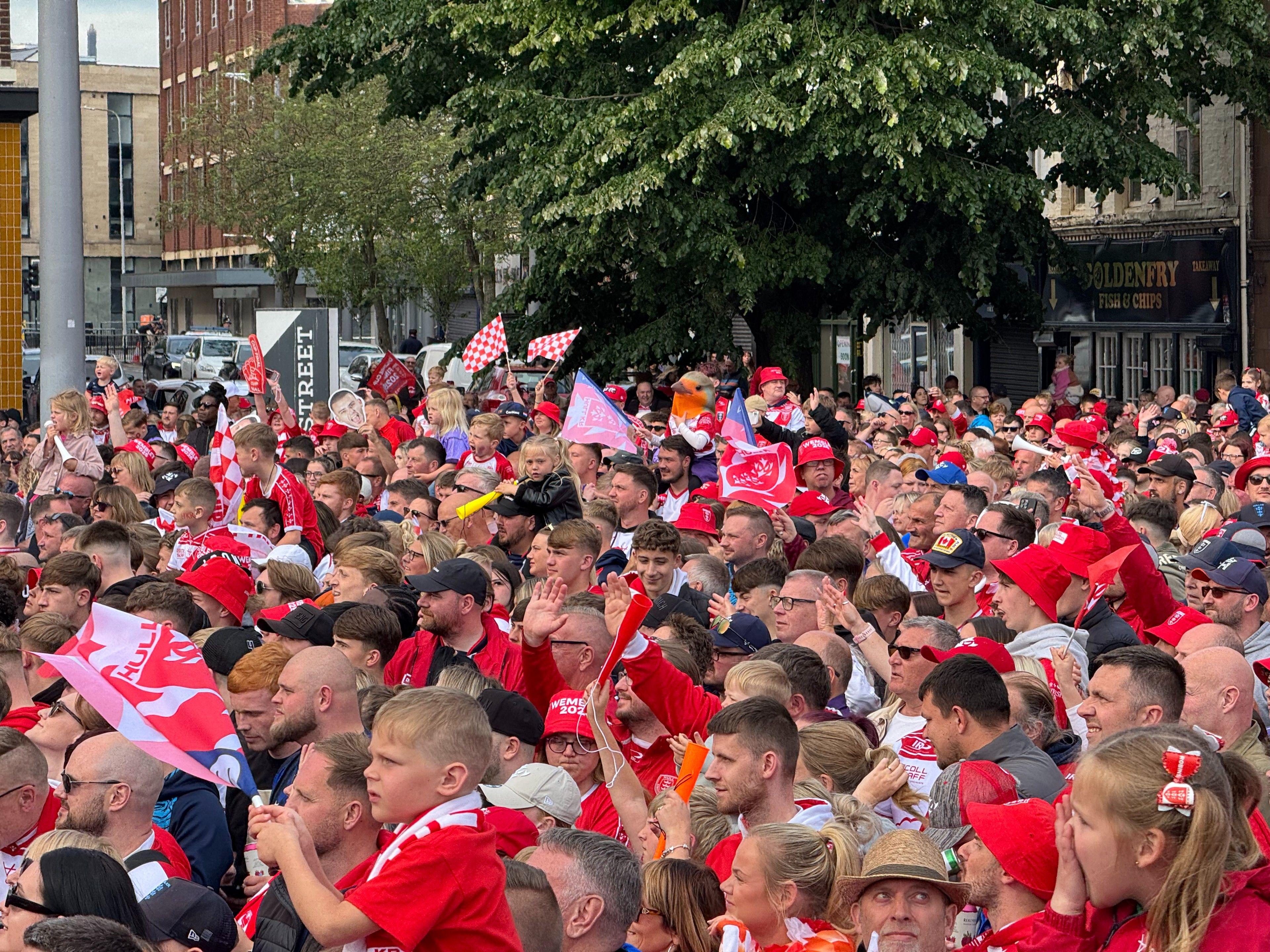 A large crowd looks towards Hull City Hall. One has a costume robin bird on his head and many are waving flags and scarves.