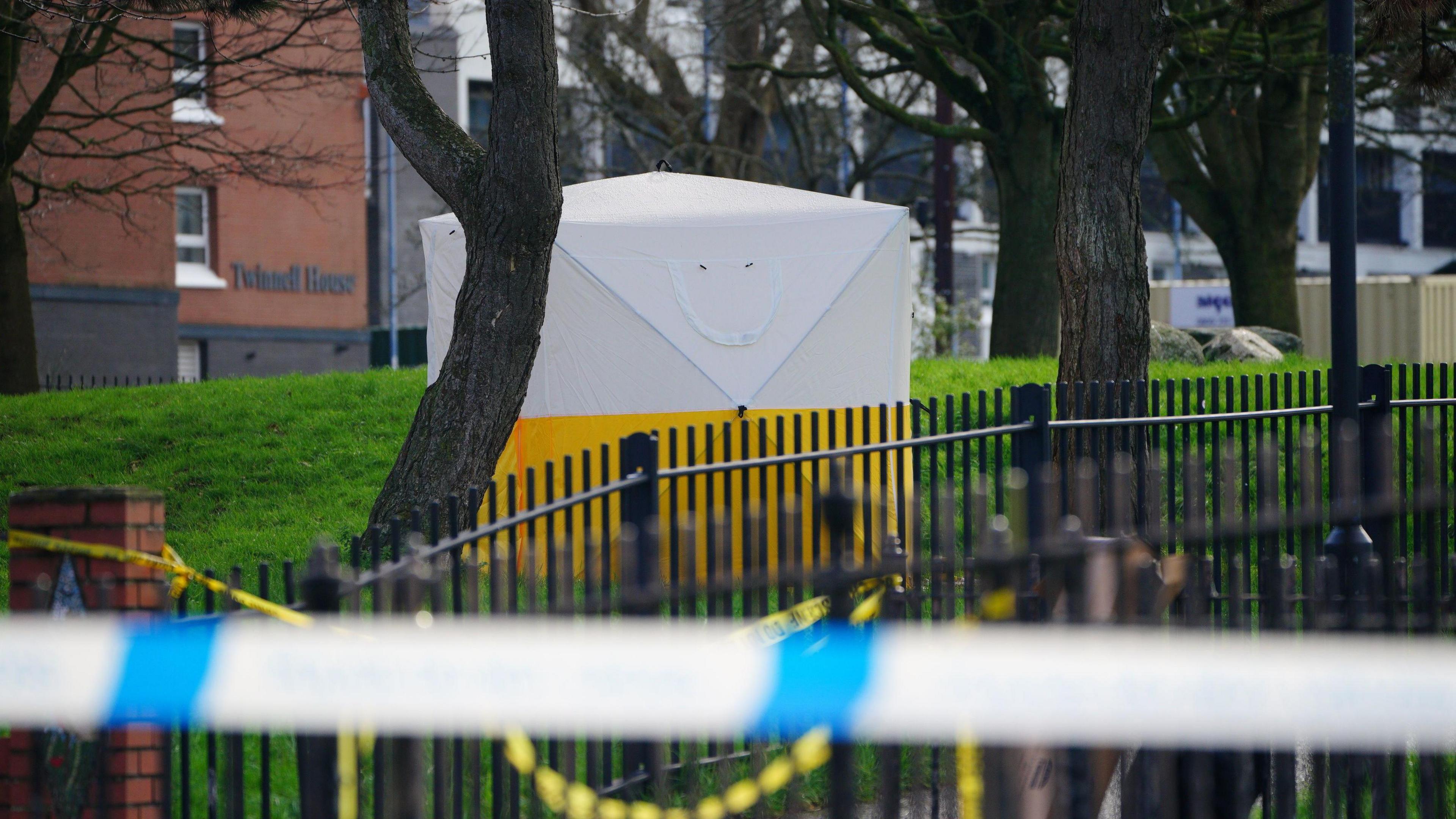 A yellow and white forensic tent behind the railings in Rawnsley Park. There is also yellow police crime scene tape securing the area.