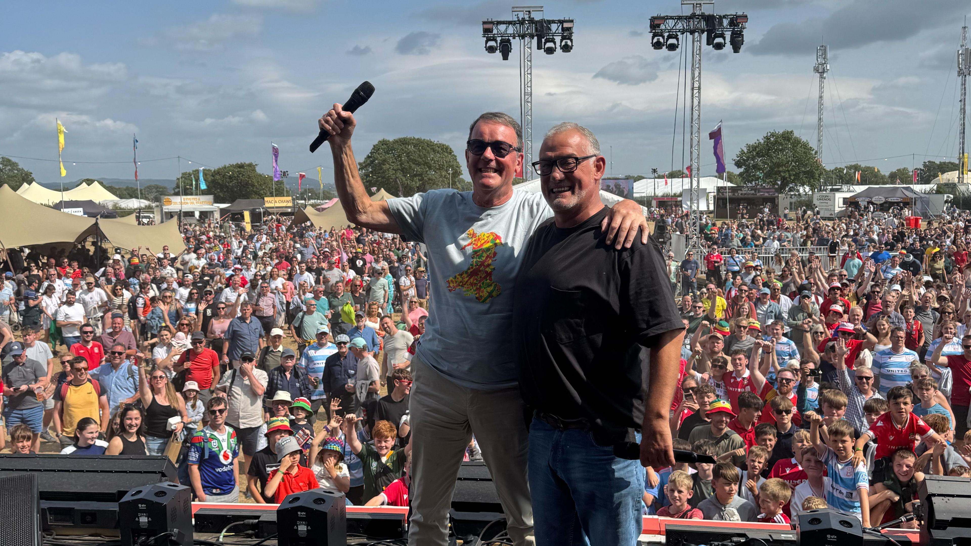 Nic Parry a Malcom Allen ar Lwyfan y Maes gyda'r dorf tu ôl iddynt