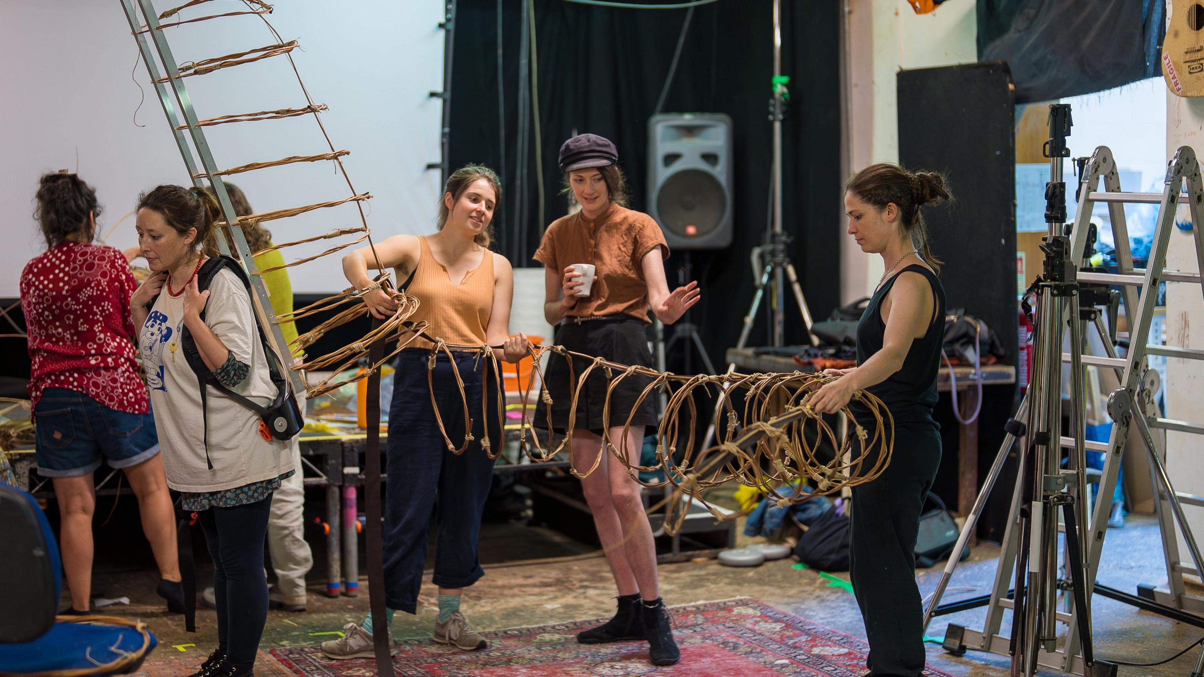 Four women gathered round the frame of a giant puppet. They are discussing how best to assemble it.