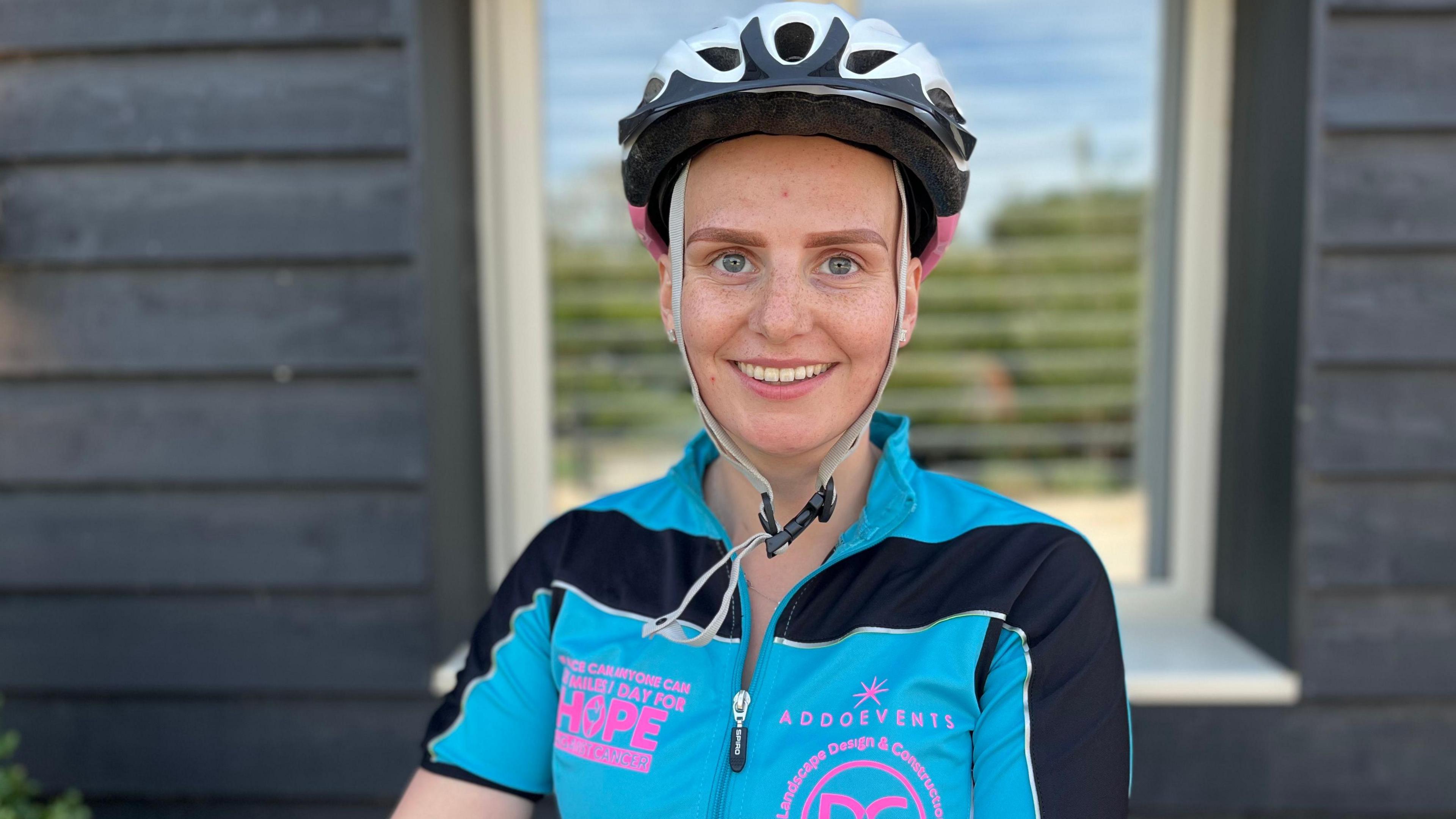 A young girl wearing a bike helmet and a blue and black jacket smiles into the camera.