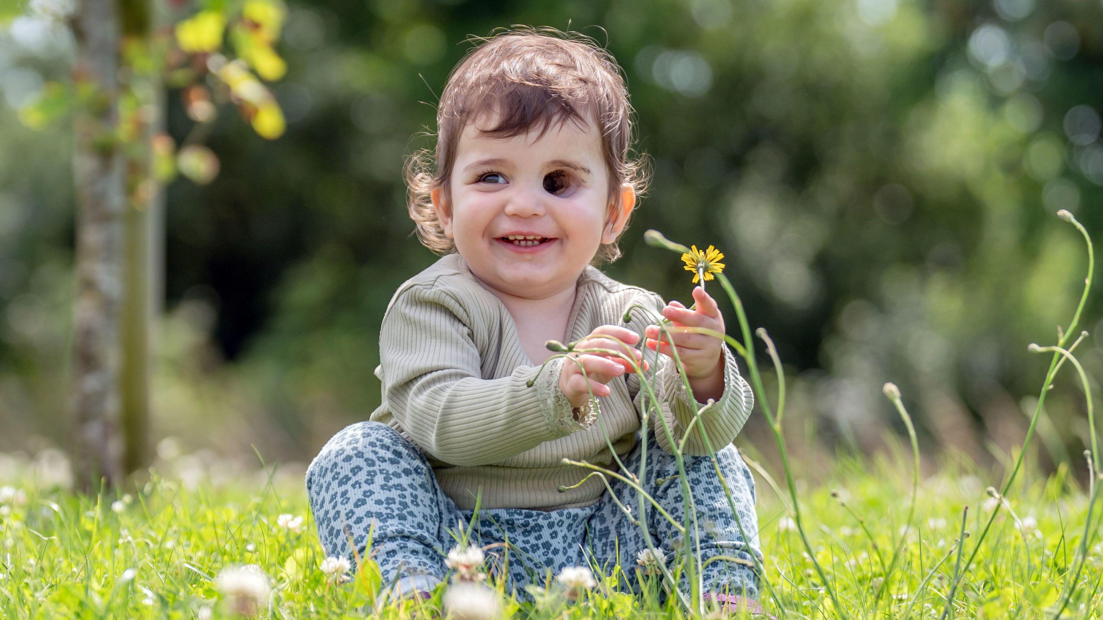 Nuala Mulholland holding a flower sitting in a field and smiling to the left of the camera