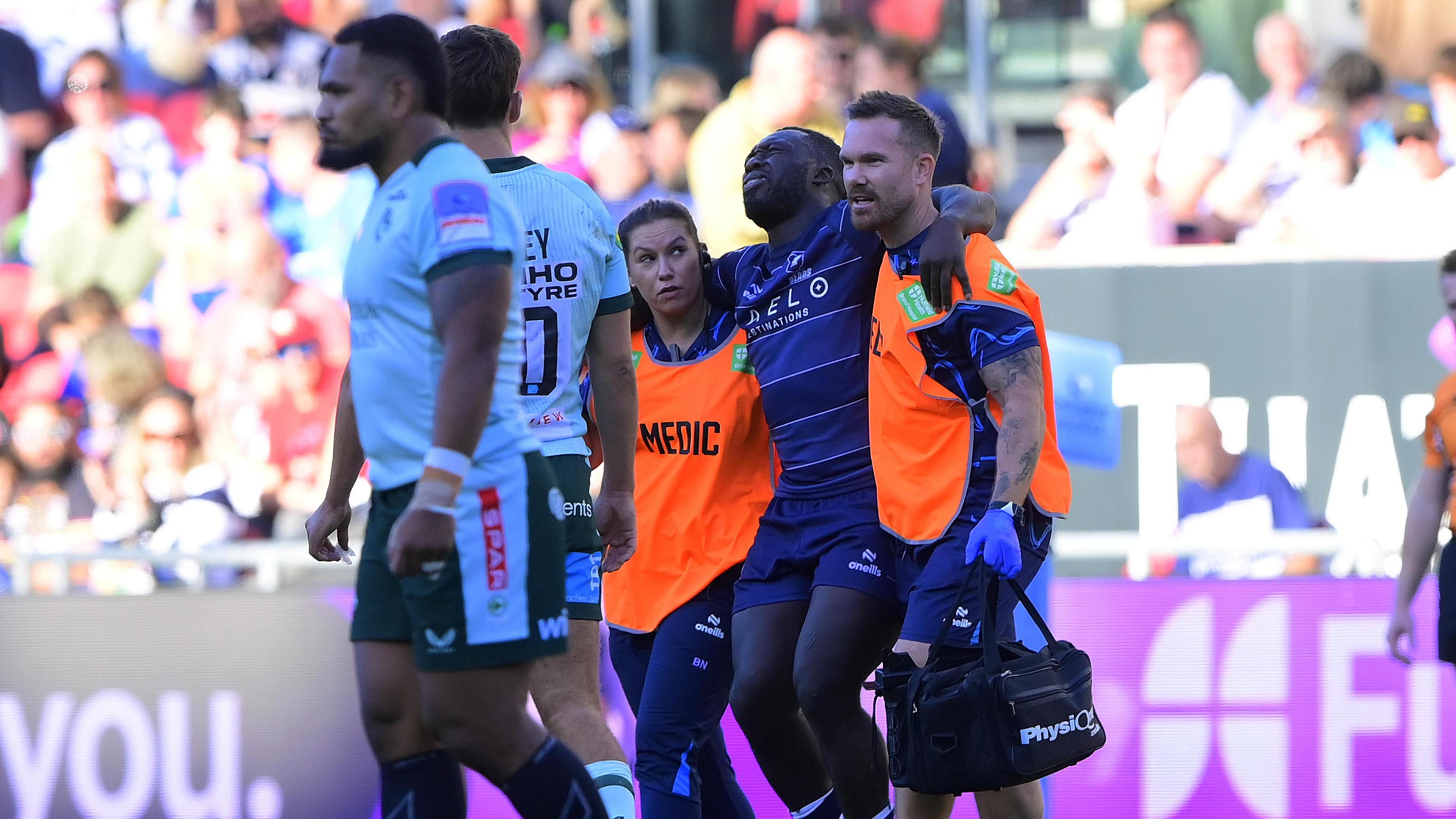 Gabriel Ibitoye is helped off the pitch by two medics 