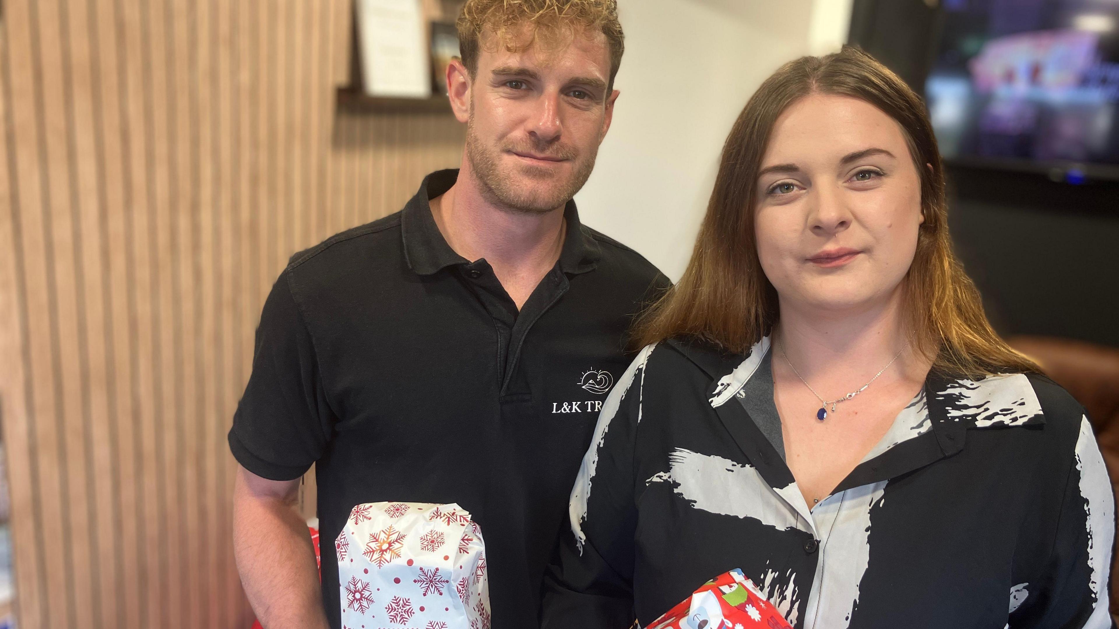 A man and woman with black clothing smiling at the camera while holding presents