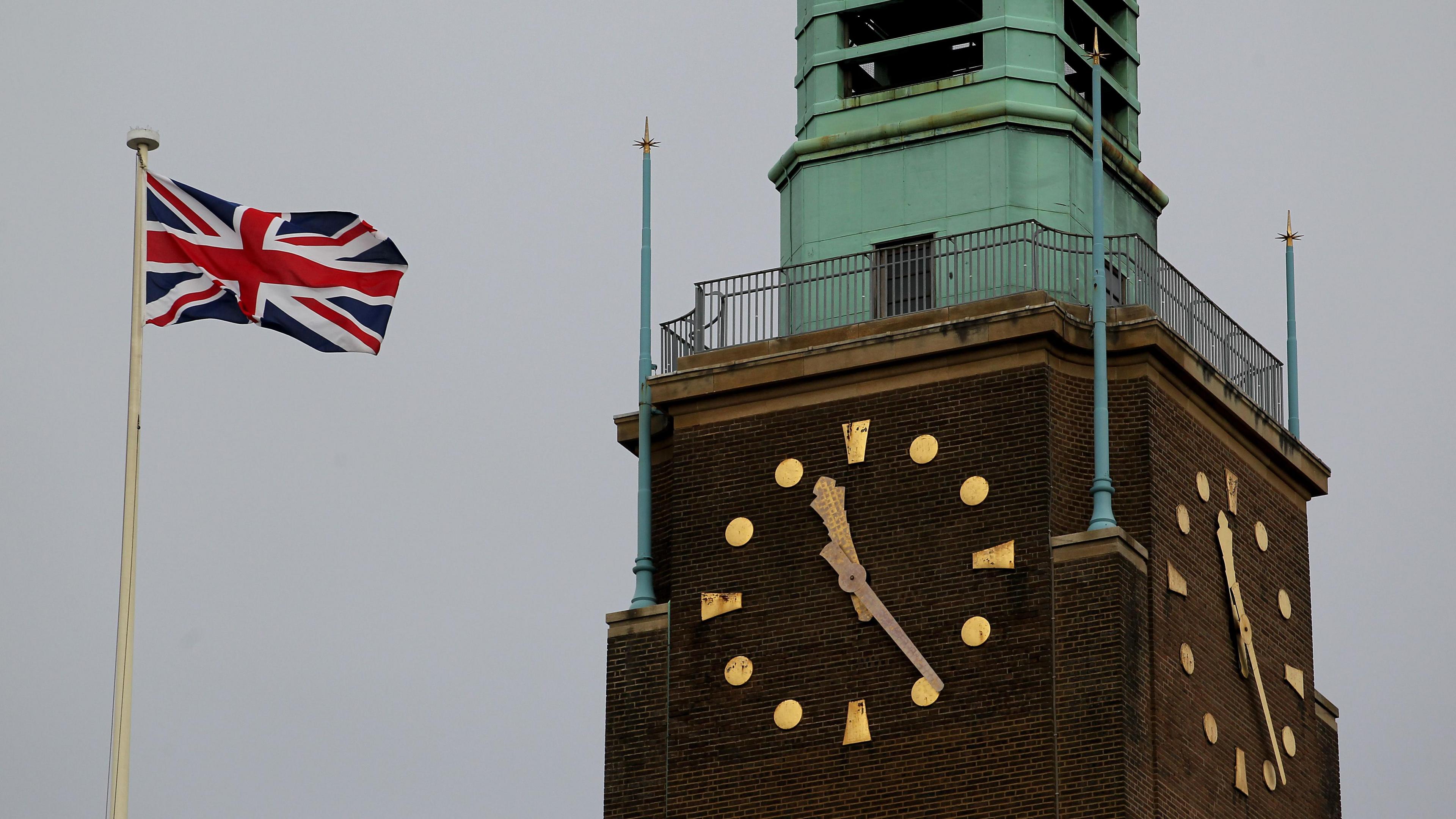 Clock tower of Norwich City Hall depicting the dial at 11.25am, alongside a Union Jack flag.