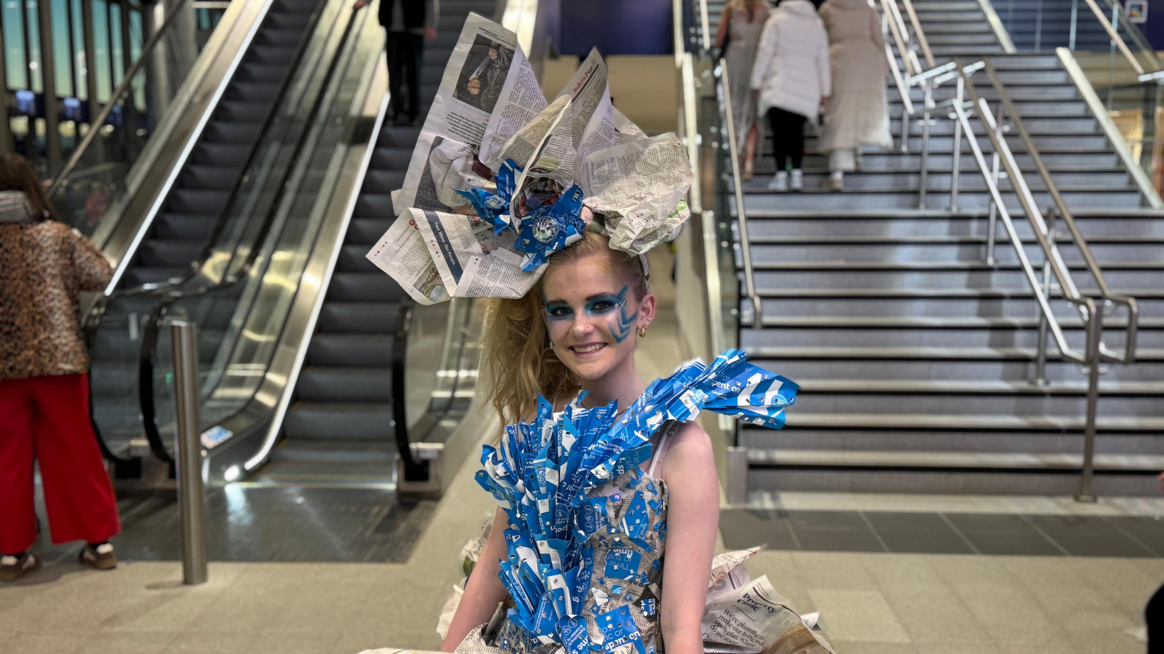 Aoife wearing an outfit made out of newspapers, old train tickets and plastic sheets. The dress also has a large hat piece. 