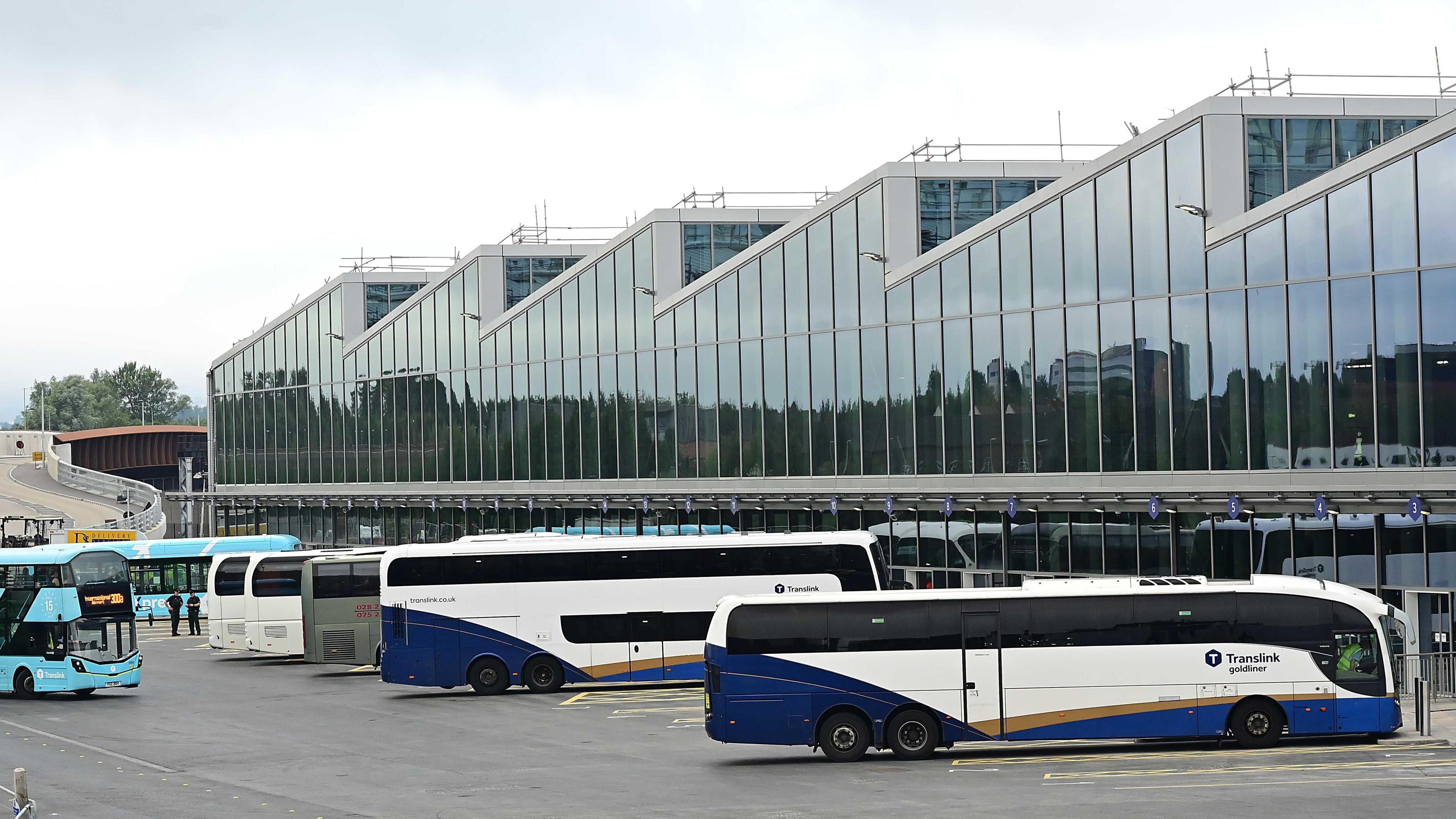 Translink buses are lined up outside the station. An airport express bus is arriving. The building is surrounded by windows and the roof is a wave shape.