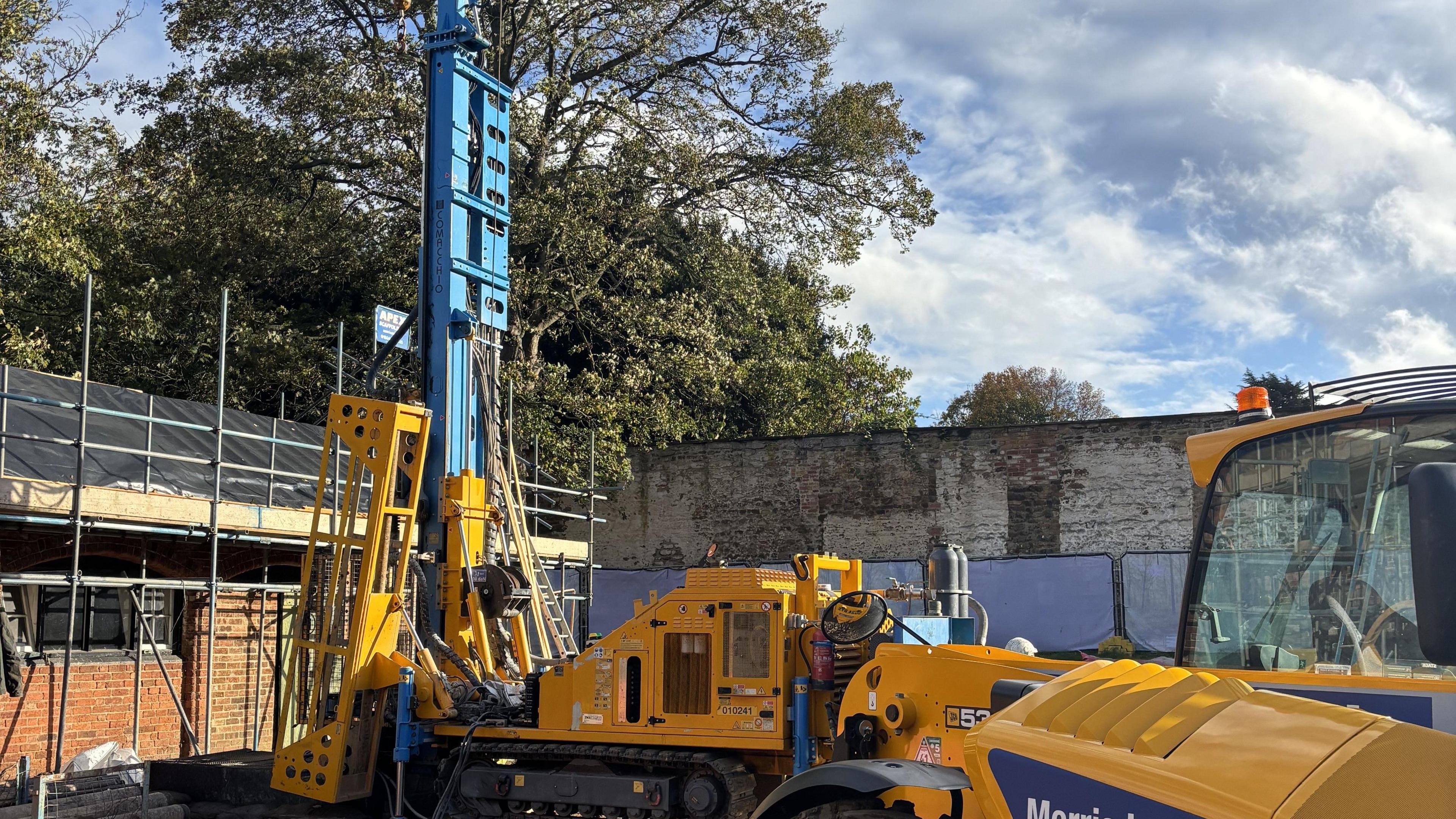 Yellow construction machinery sits dormant next to brick walls with metal scaffolding. 