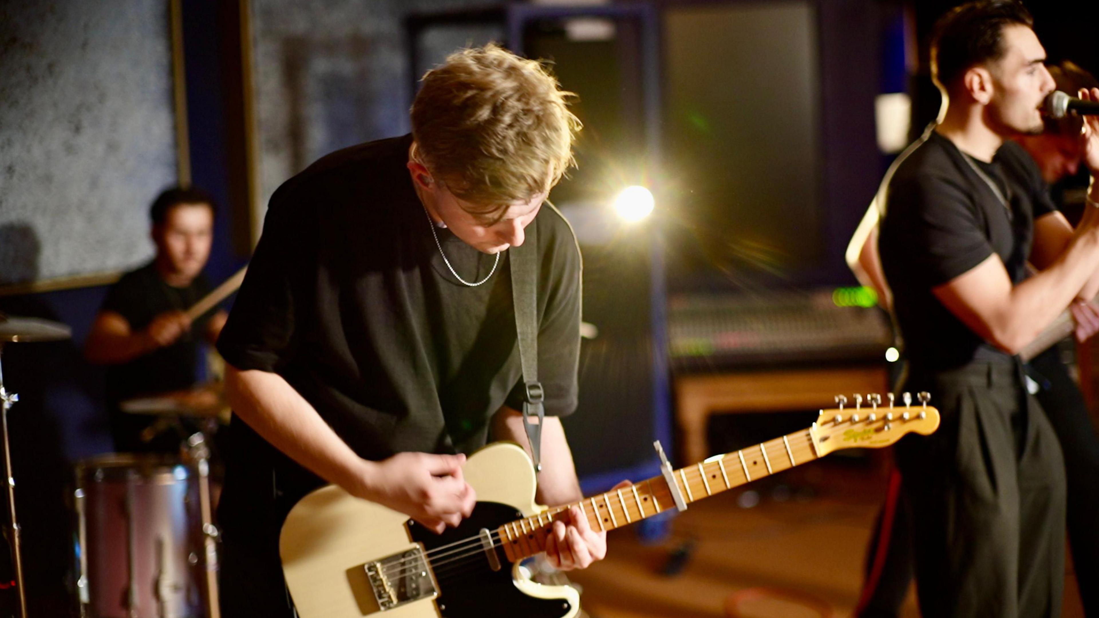 Guitarist Luke Ellis, mid strumming his electric guitar which is two tone white and black. 