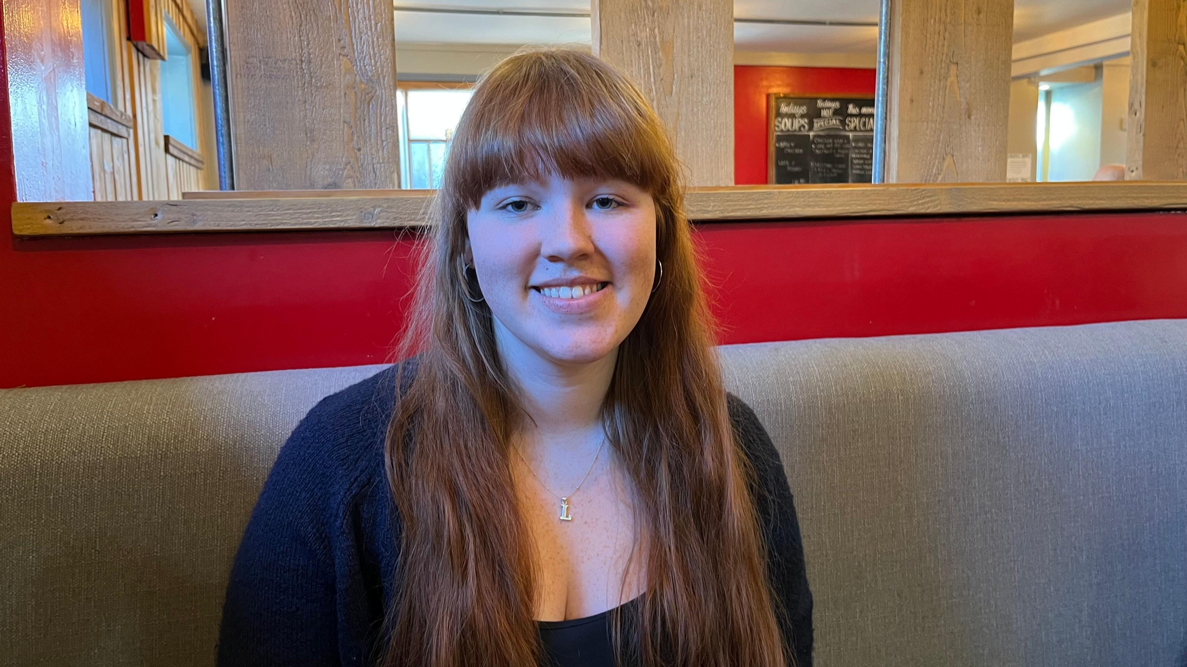 Latonya Skye-Patterson, a 20-year-old woman with long, auburn hair sits in a cafe looking at the camera
