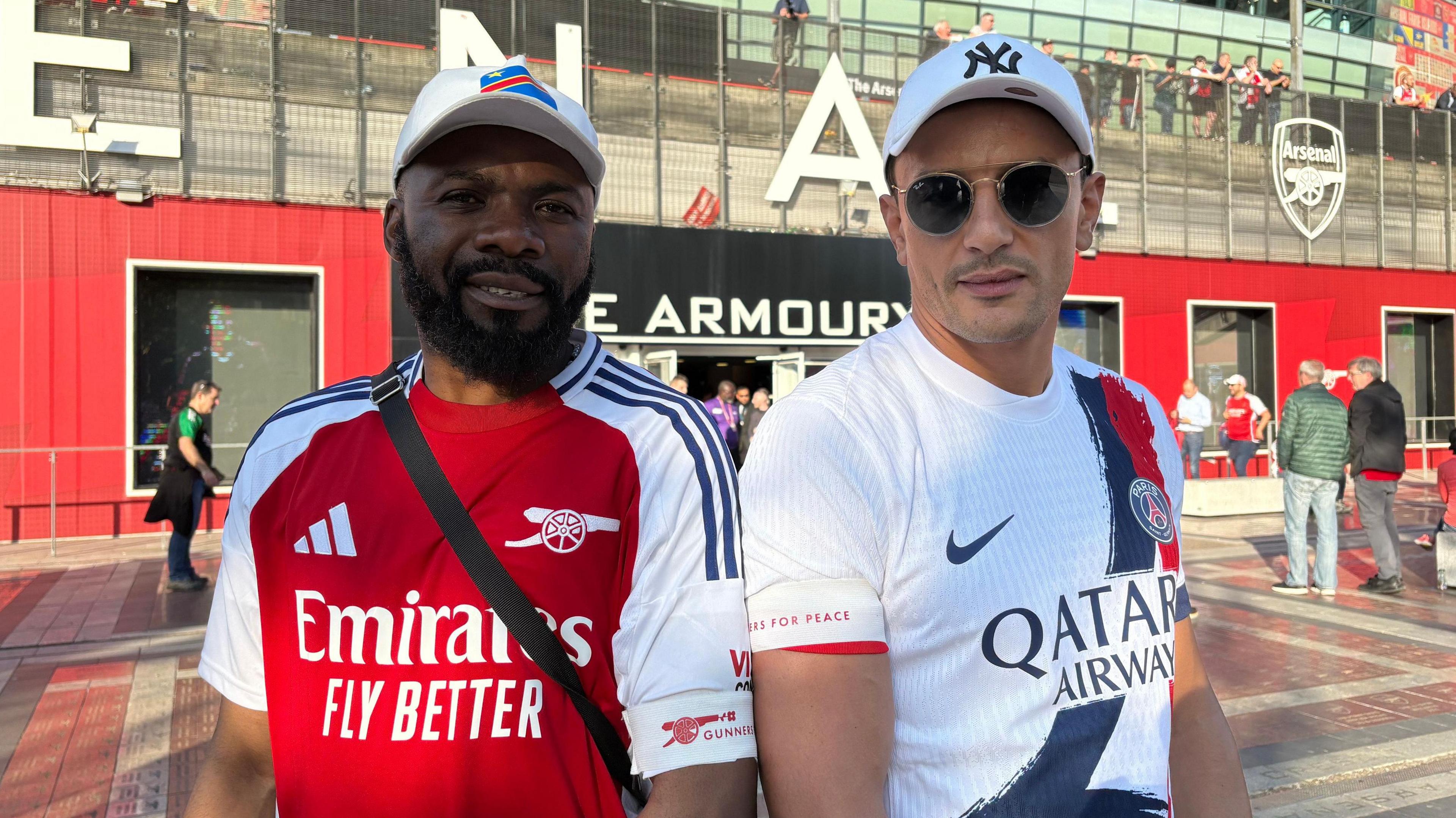 Arsenal fan Tresor Kudabika and PSG fan Chakib pose outside of the Emirates Stadium wearing Gunners for Peace armbands over their football shirts