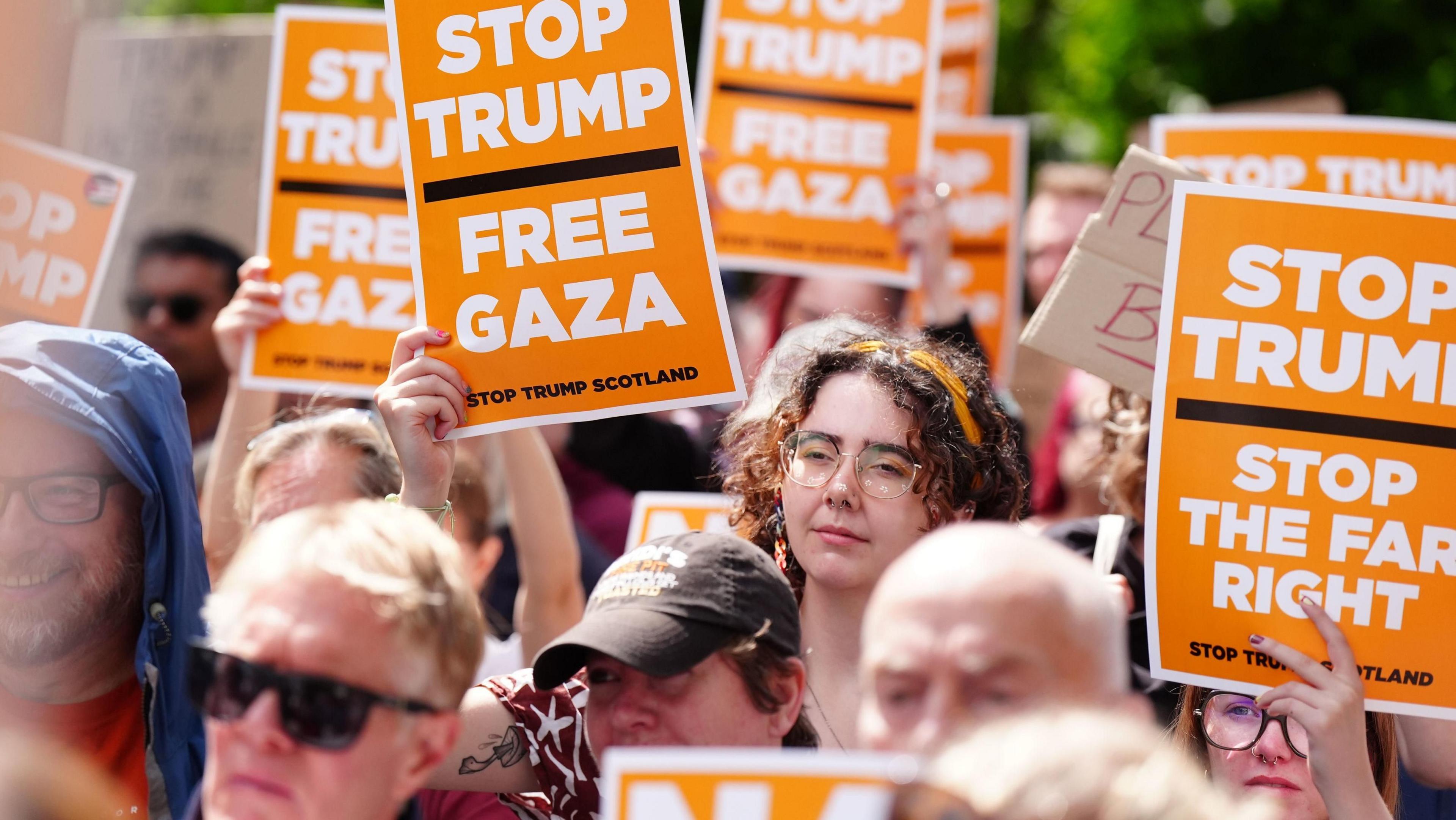 A crowd of anti-Trump protesters with orange signs bearing slogans including "Stop Trump Free Gaza"