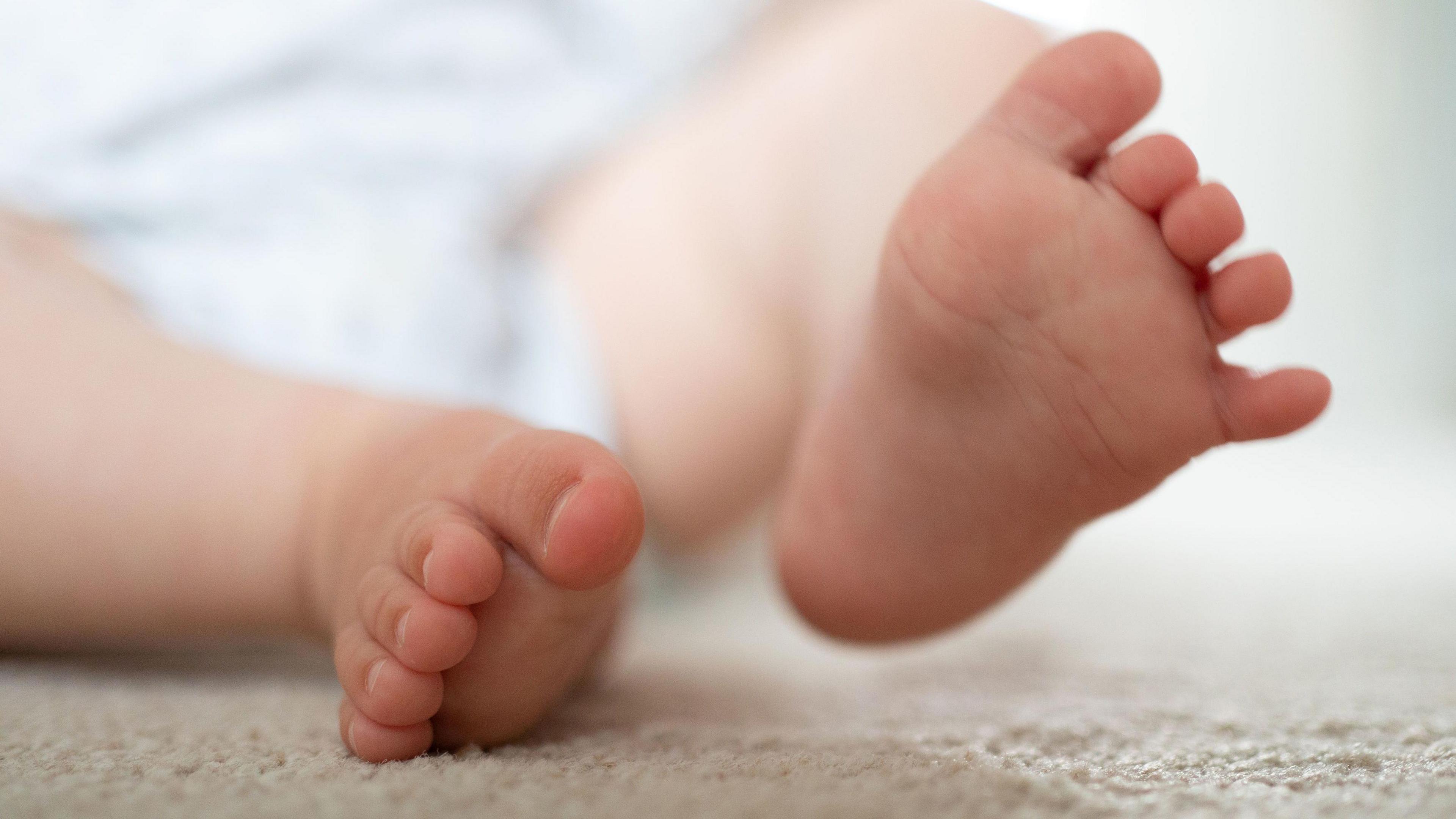 Close-up of two small bare feet resting on a soft, light-colored surface, with toes slightly curled and background softly blurred