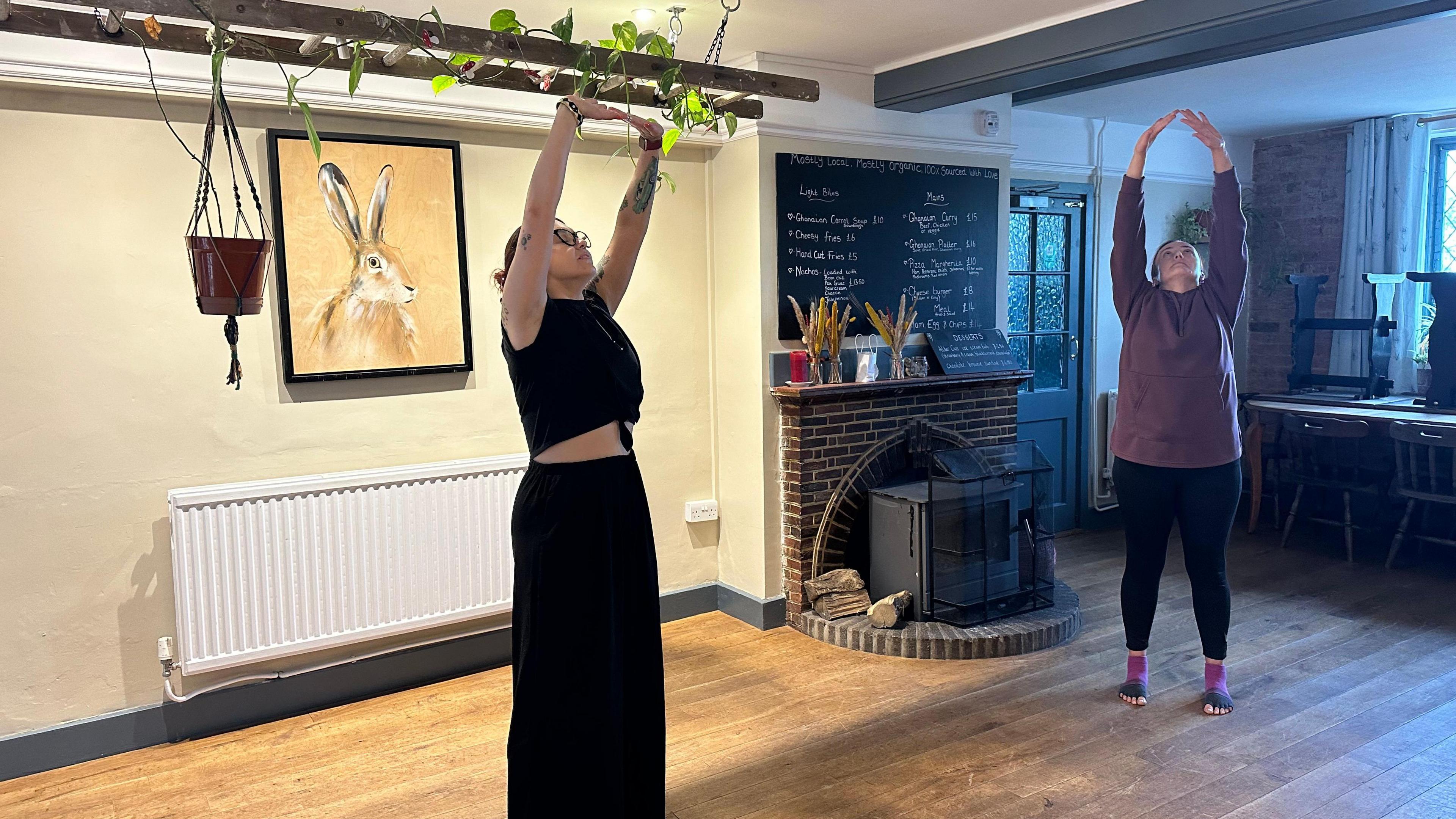 The group stand together stretching upwards to the ceiling, breathing slowly in a meditative rhythm  