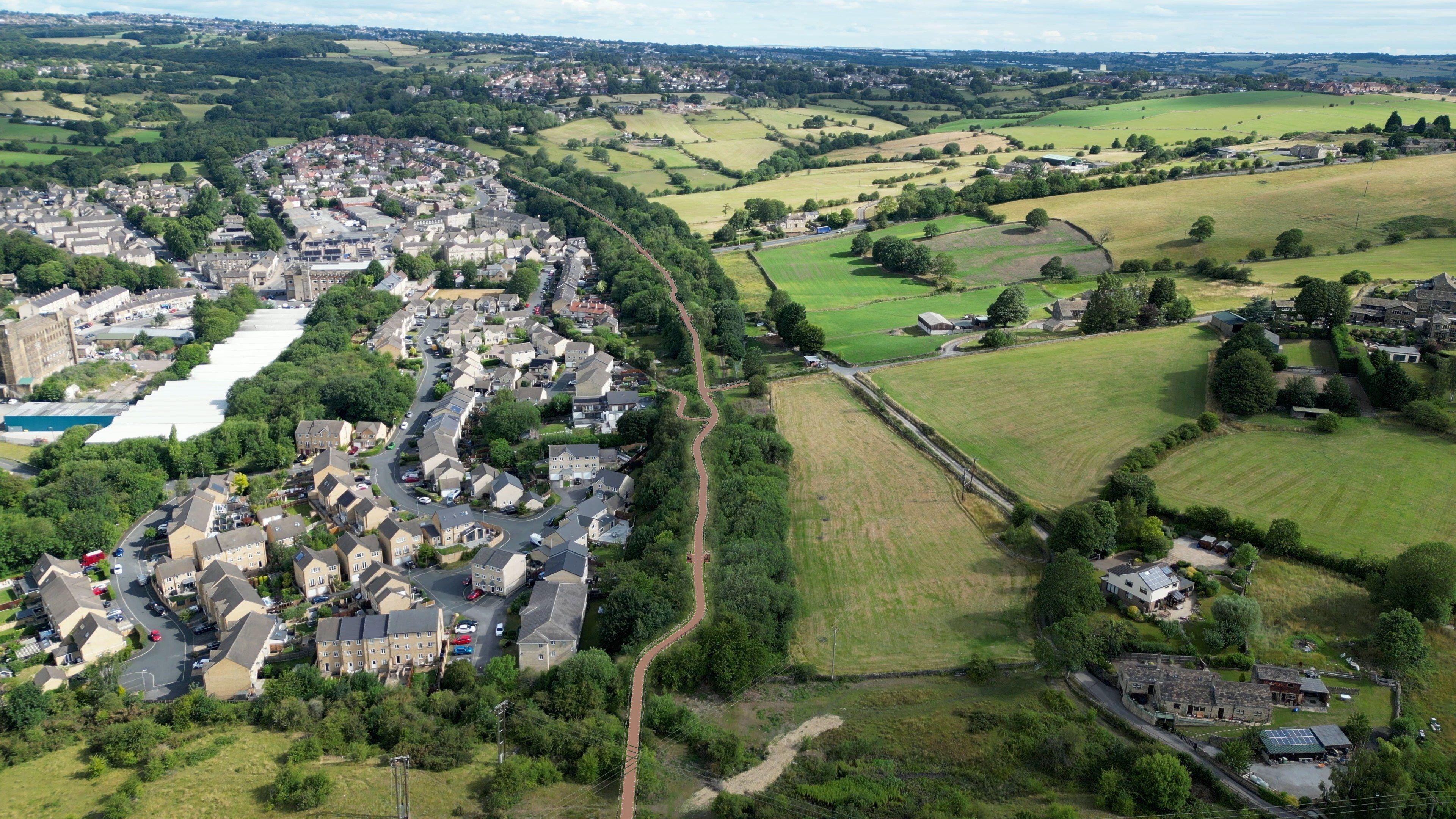 A CGI image showing a long brown path running alongside a small town. The birds-eye view also captures green fields and farmland to the right.