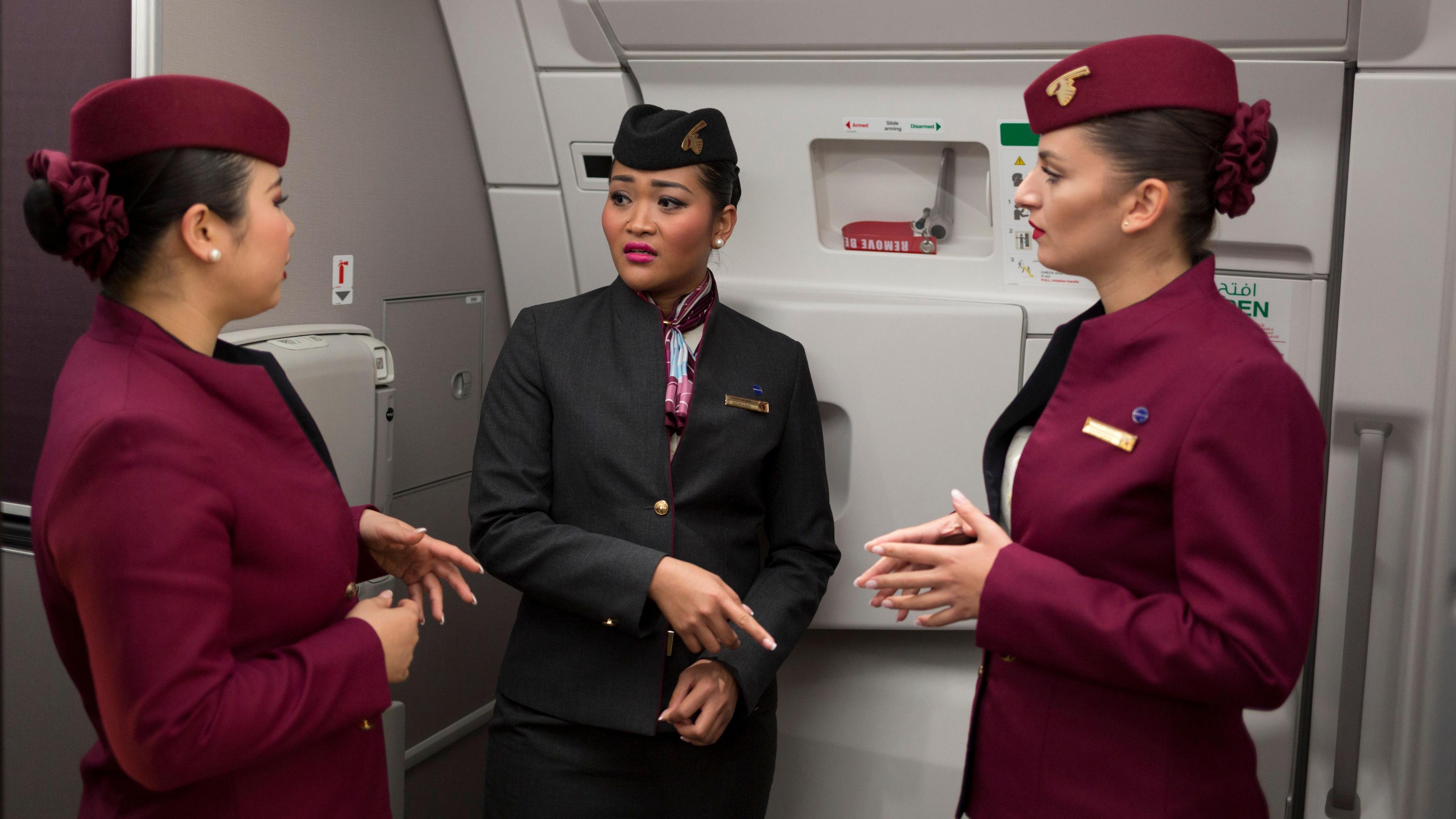 Three members of Qatar Airways cabin crew in conversation by the closed door of a plane.