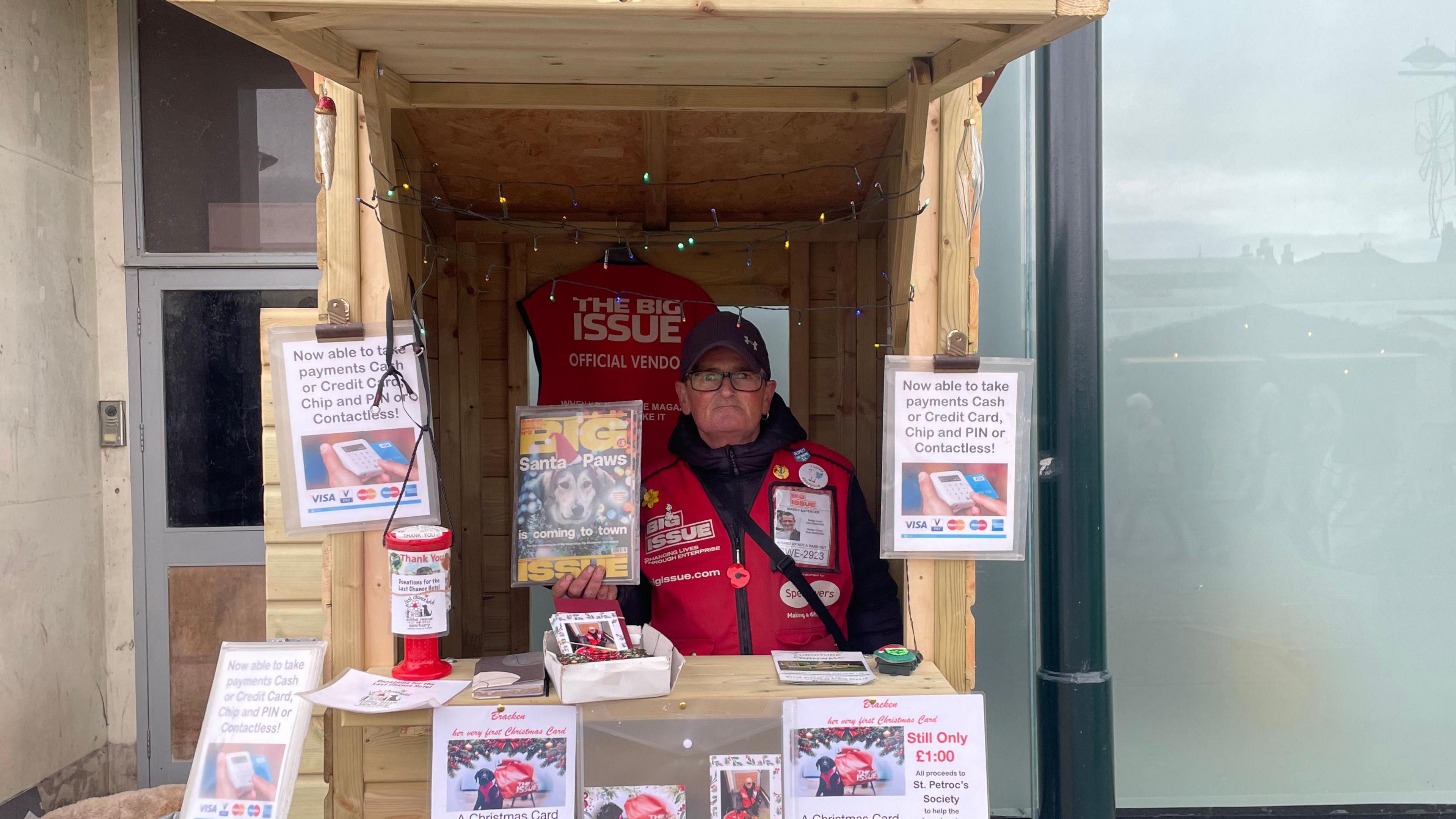 Big Issue seller in wooden shelter 