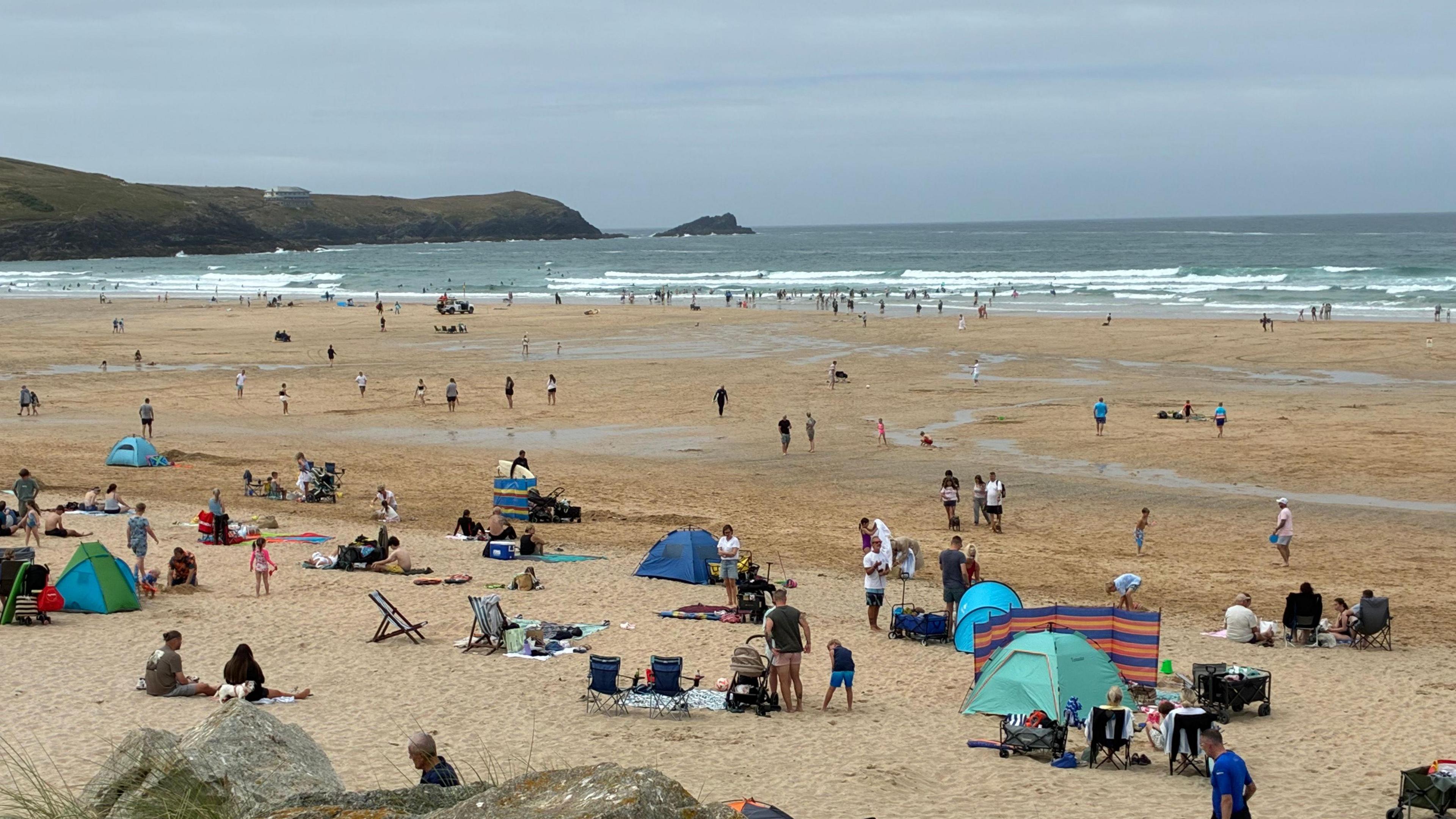 A wide sandy beach with lots of people on, and in the sea